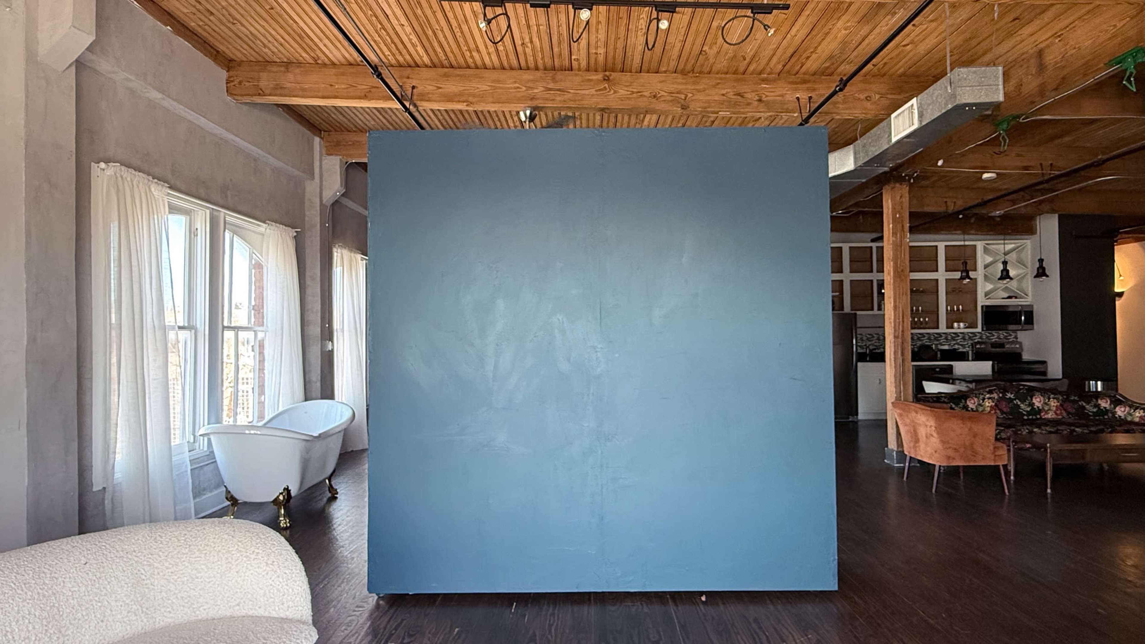The image shows an interior space featuring a large blue wall in the center, with a bathtub and seating area visible in the background.