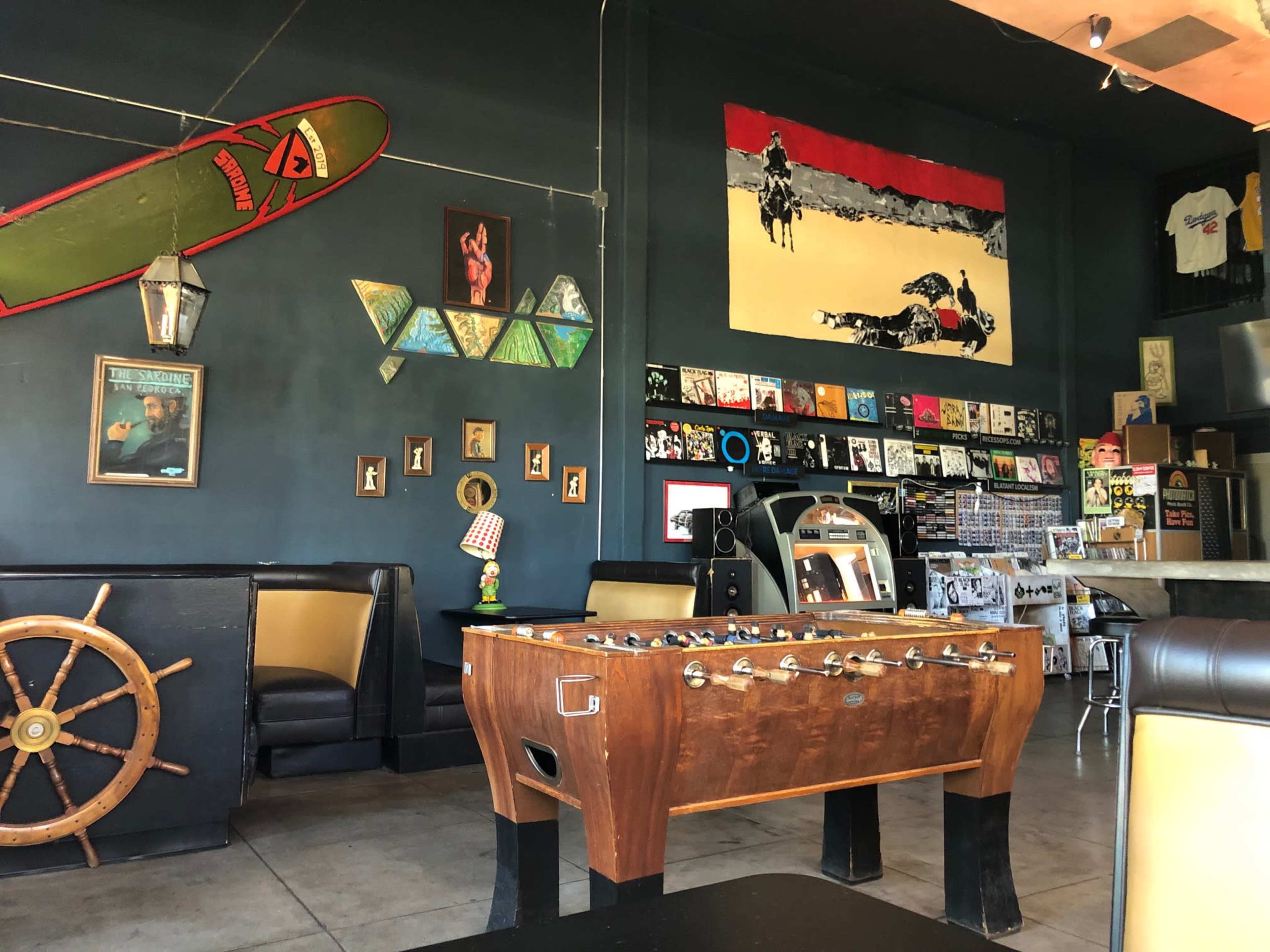 The interior of a casual bar or café featuring a foosball table, a large wall mural of a horse, and various framed artworks and records displayed on the walls.