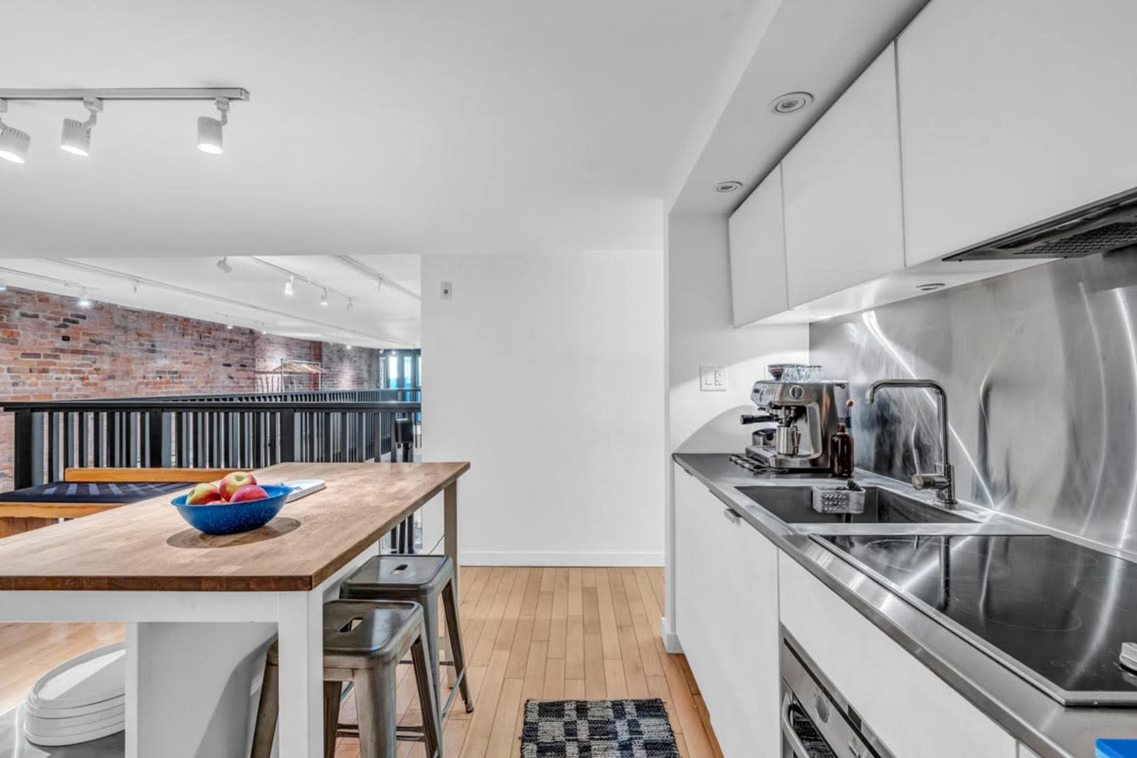 A modern kitchen area with stainless steel appliances, a wooden island, and a bowl of fruit on the countertop.