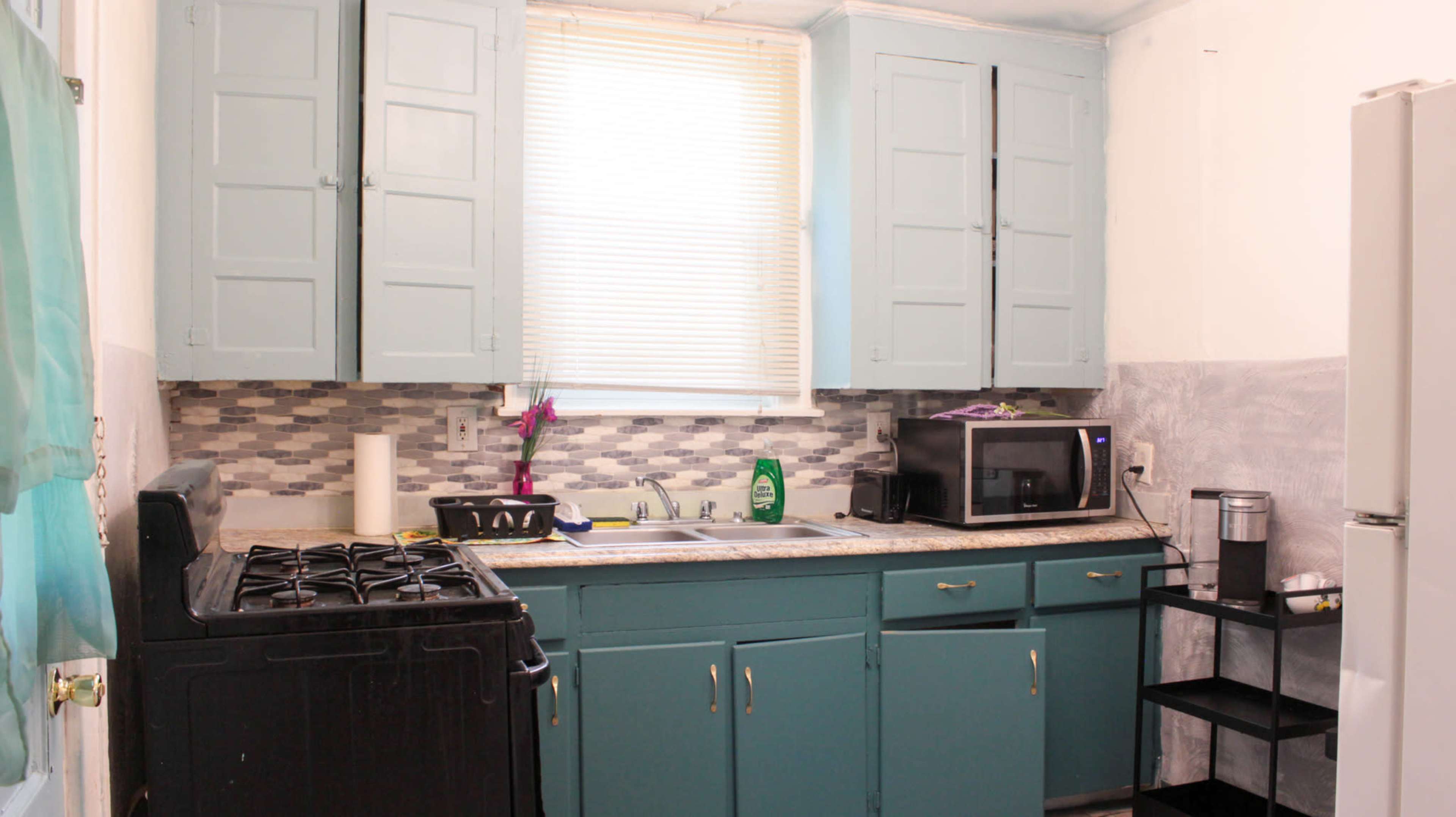 A small kitchen with blue cabinets, a gas stove, a microwave, and a stainless steel refrigerator.
