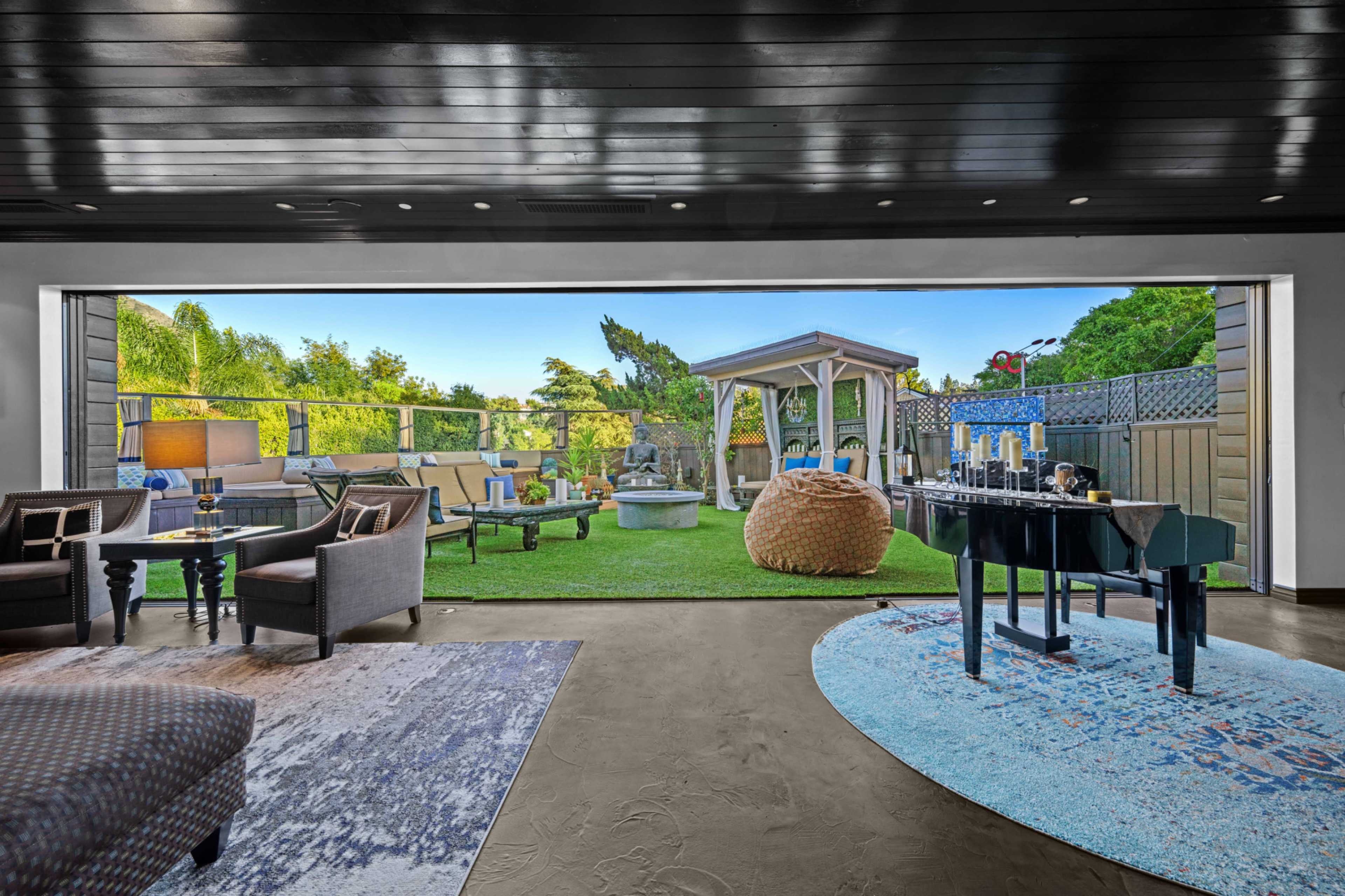 A spacious indoor living area overlooking a well-maintained outdoor patio with seating, a gazebo, and lush greenery.