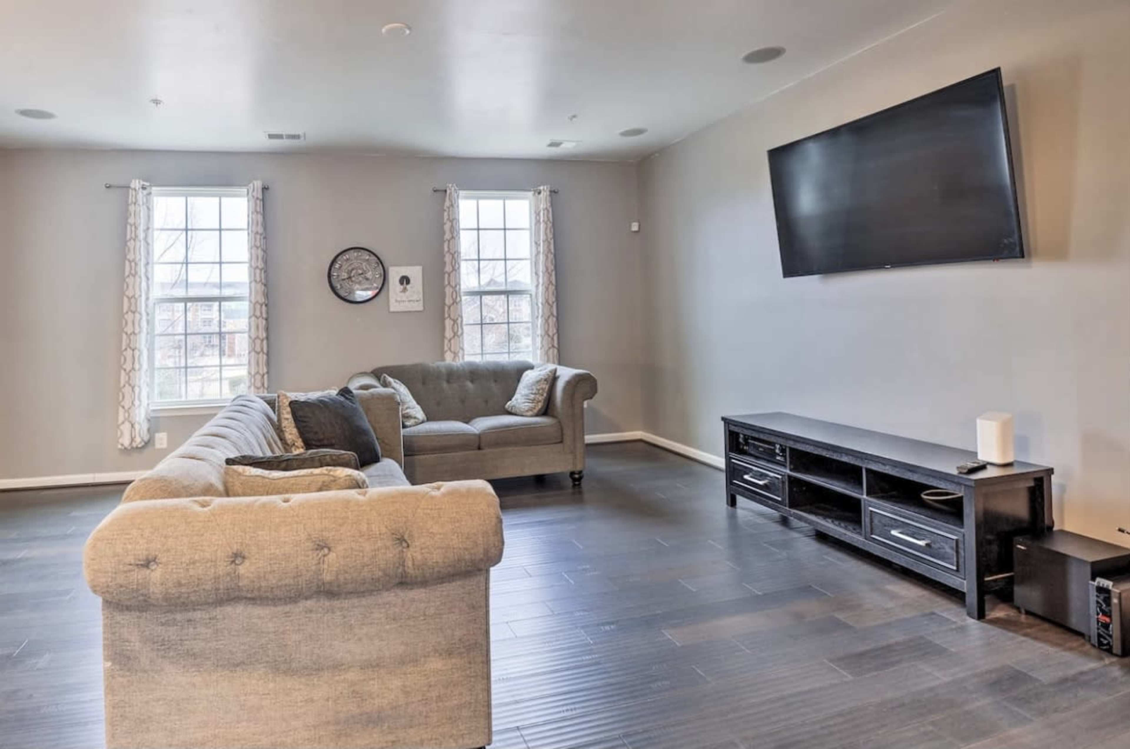 A living room with a gray sofa, a dark media console, and a wall-mounted television.