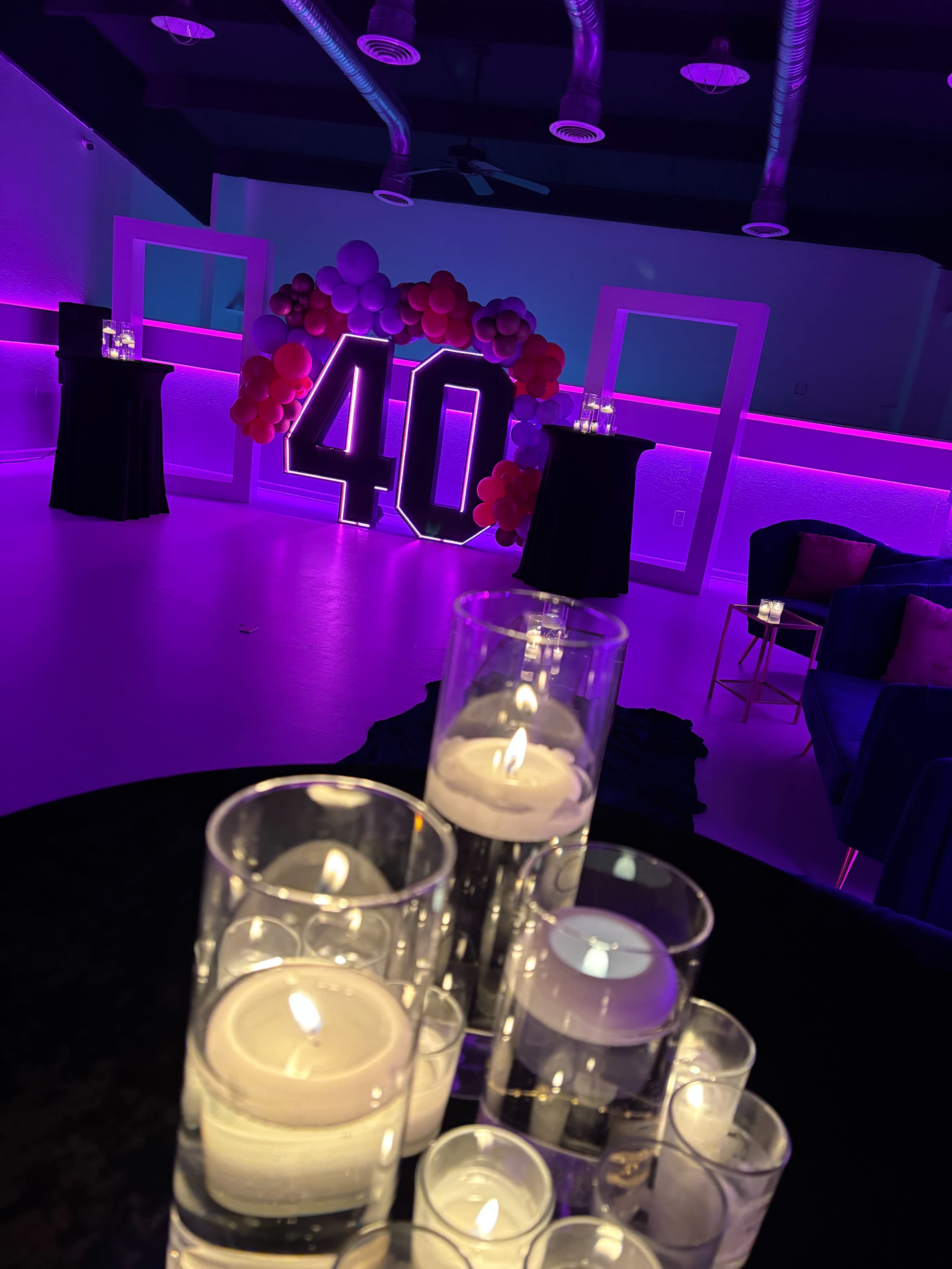 The image shows a decorated event space featuring a large "40" display made of balloons, with purple lighting and candles on tables.