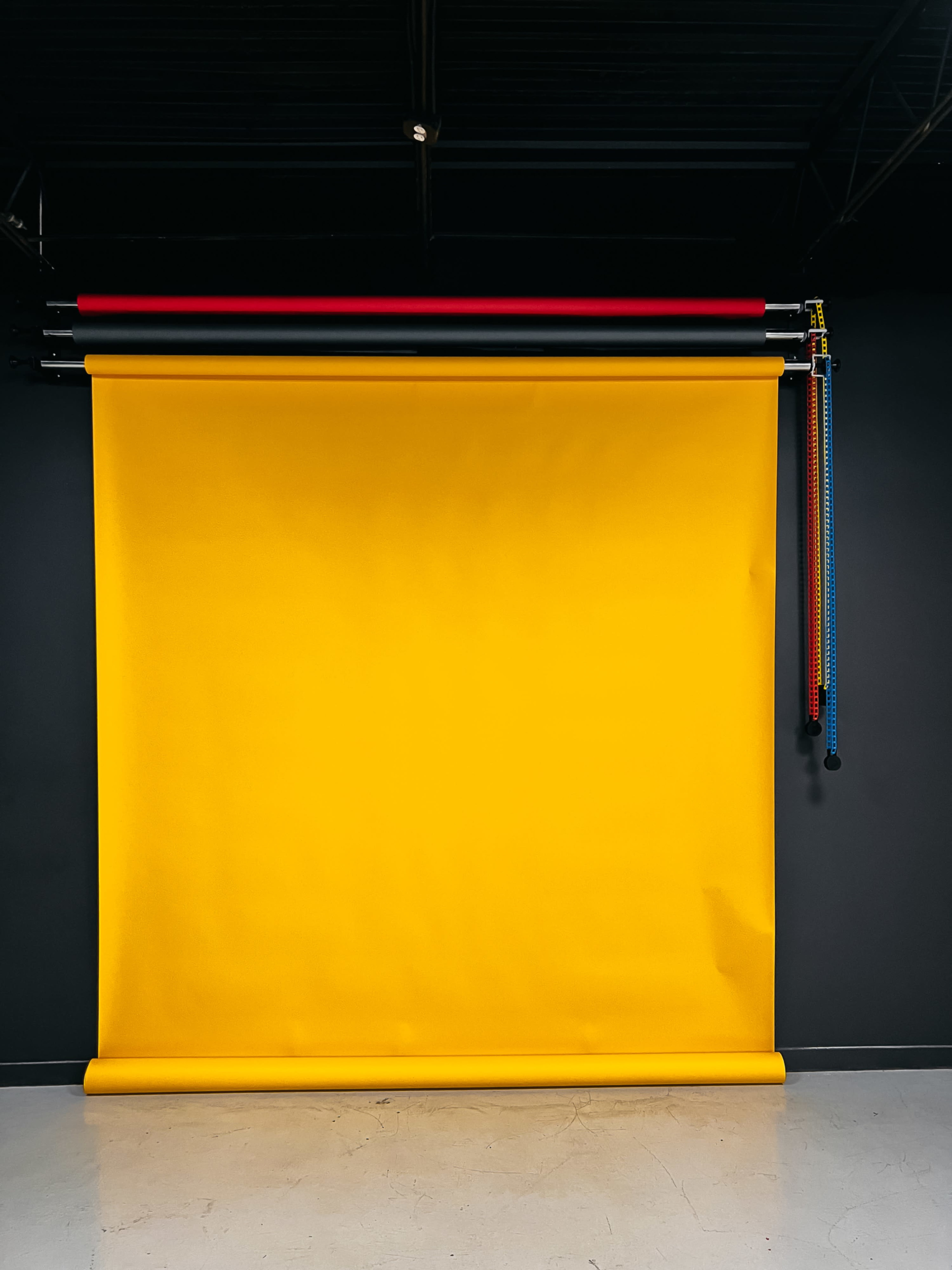 A bright yellow backdrop is rolled down against a black wall, with colorful pipes hanging above it.