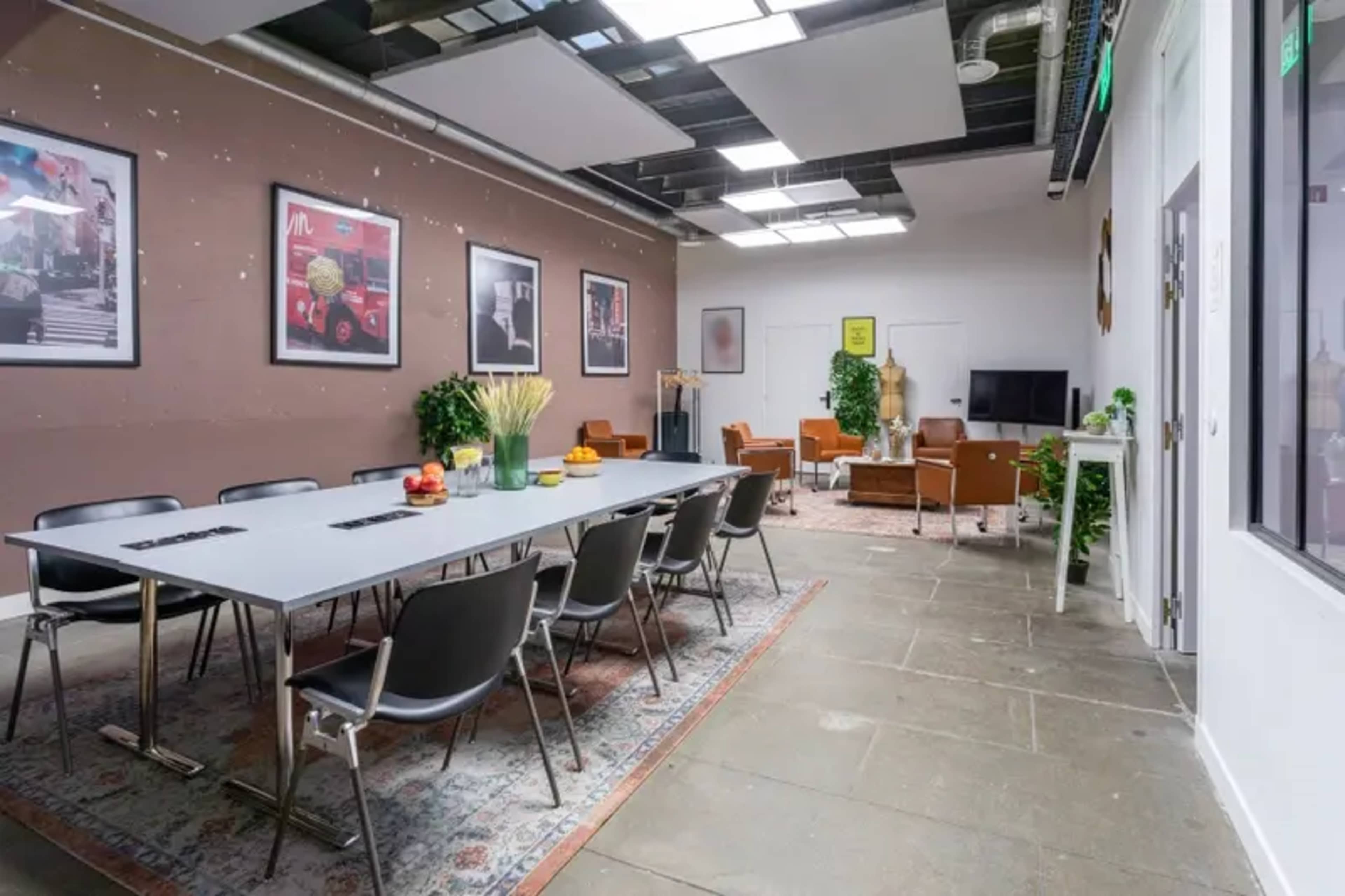 A modern meeting room features a long table surrounded by chairs, with artwork on the walls and a lounge area in the background.