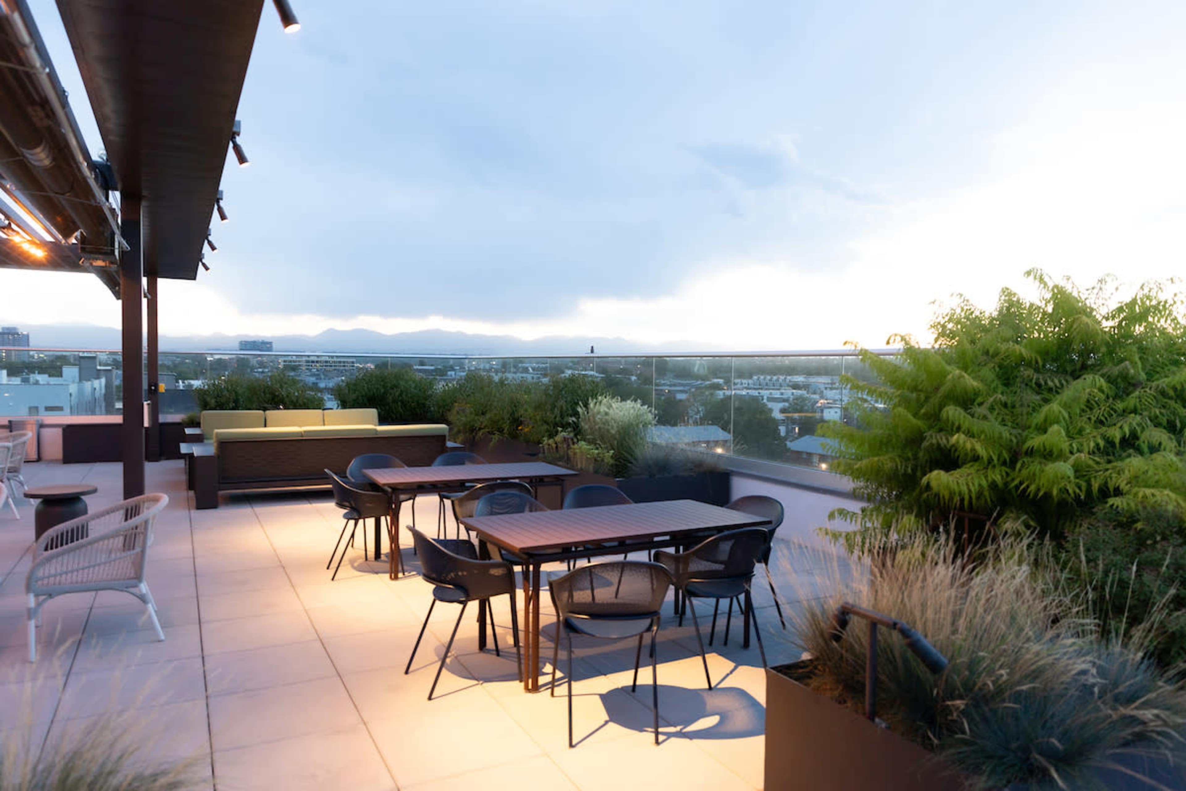 A rooftop patio features several tables and chairs with a view of distant mountains and a partially cloudy sky.
