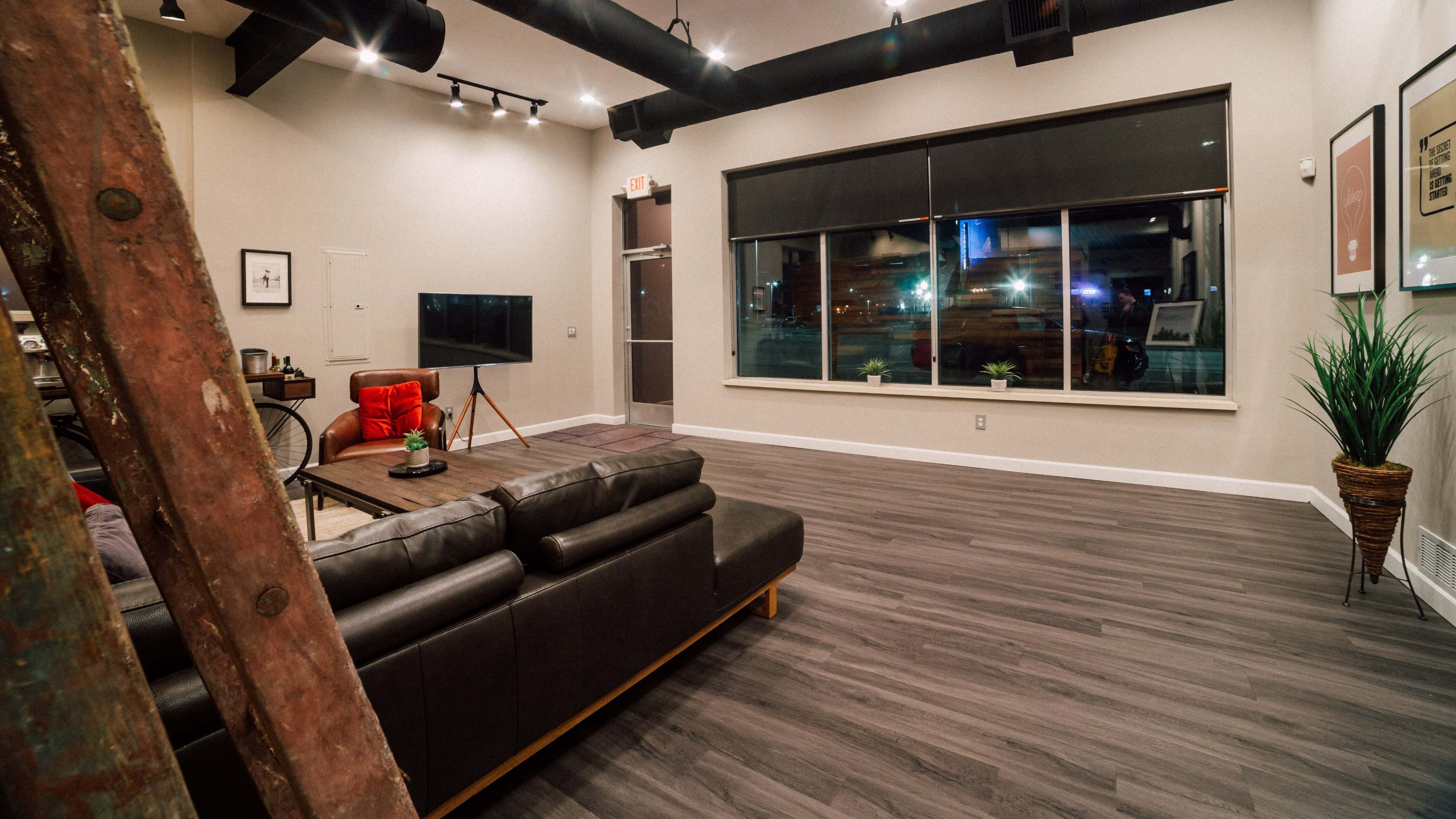 A modern interior living area with a leather sofa, a coffee table, a red armchair, and a large window overlooking the street.