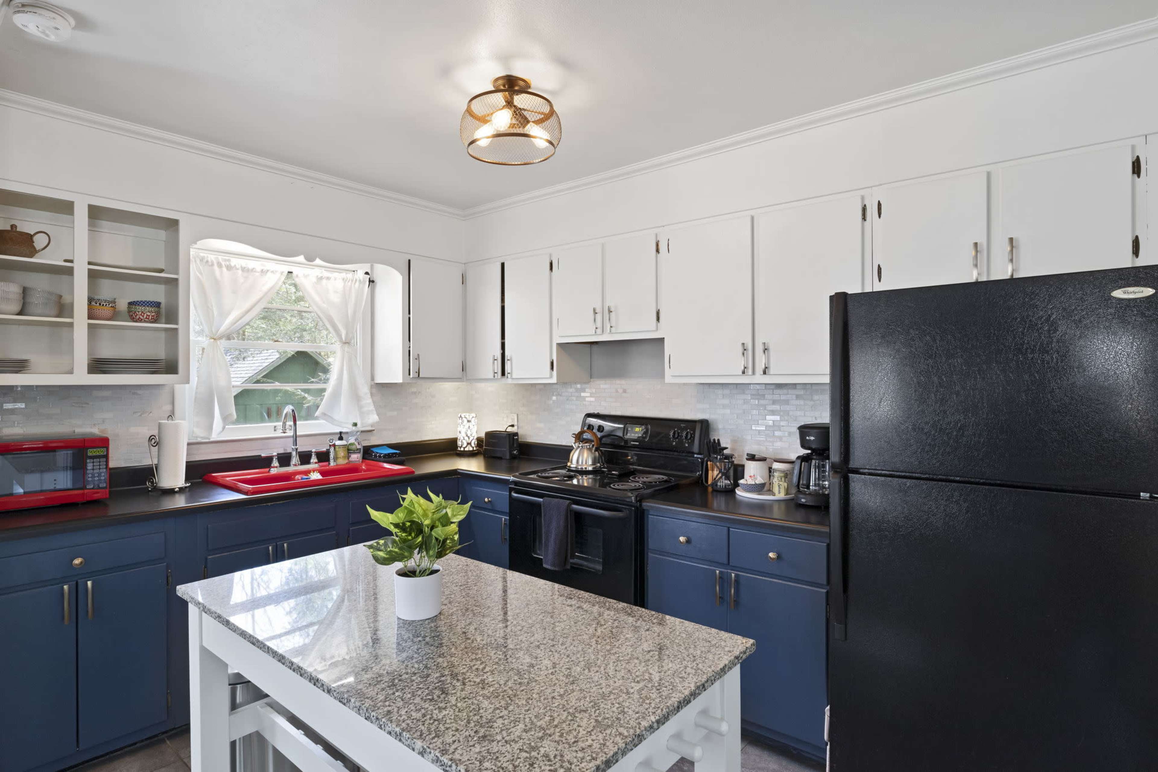 The kitchen features white cabinets, black appliances, a granite countertop island, and a window with sheer curtains.