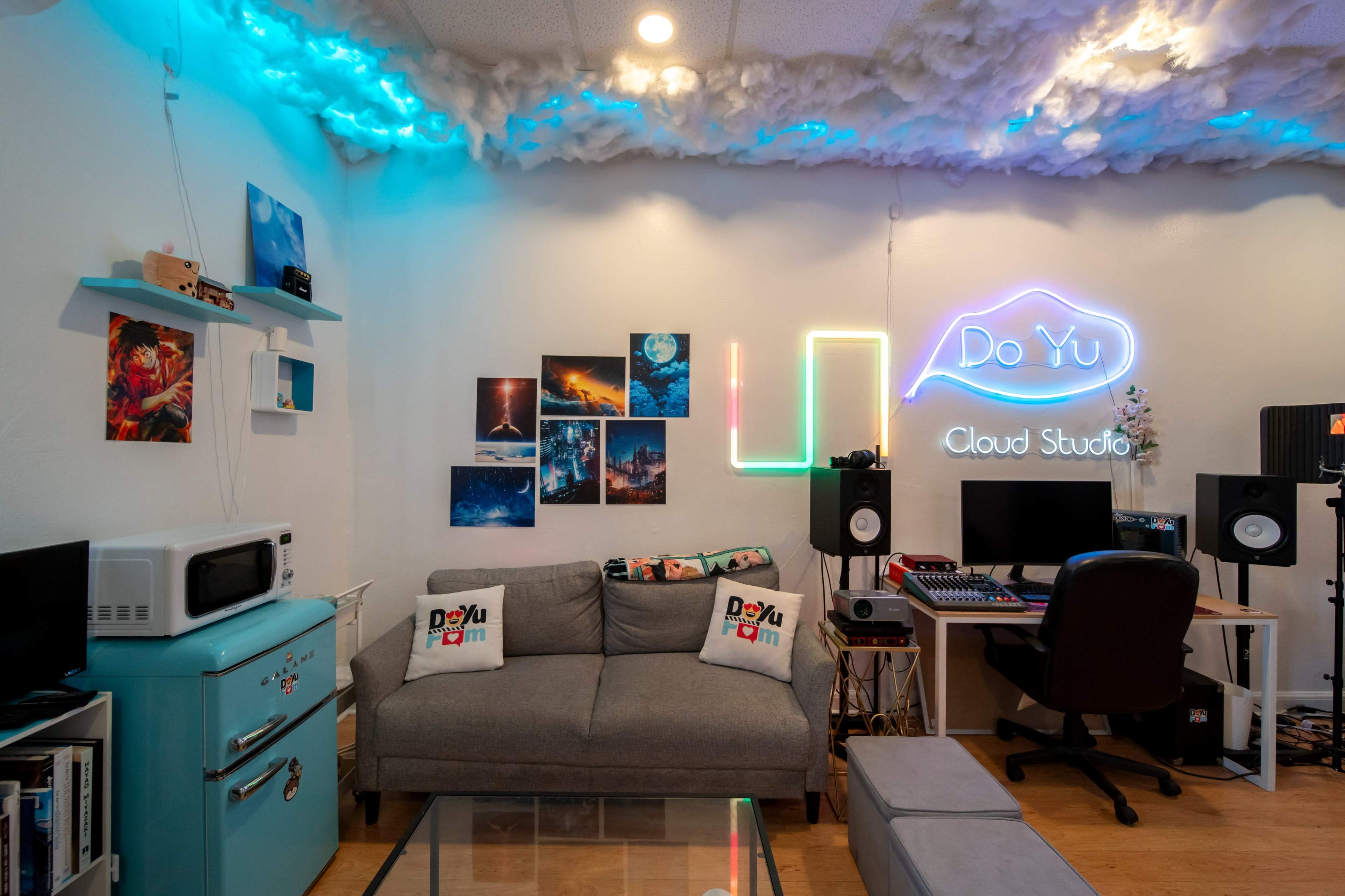 The image shows a cozy studio space designed for creative work, featuring a gray couch, a neon sign that reads "Do Yu Cloud Studio," and vibrant wall art, all illuminated by soft, colorful lighting.