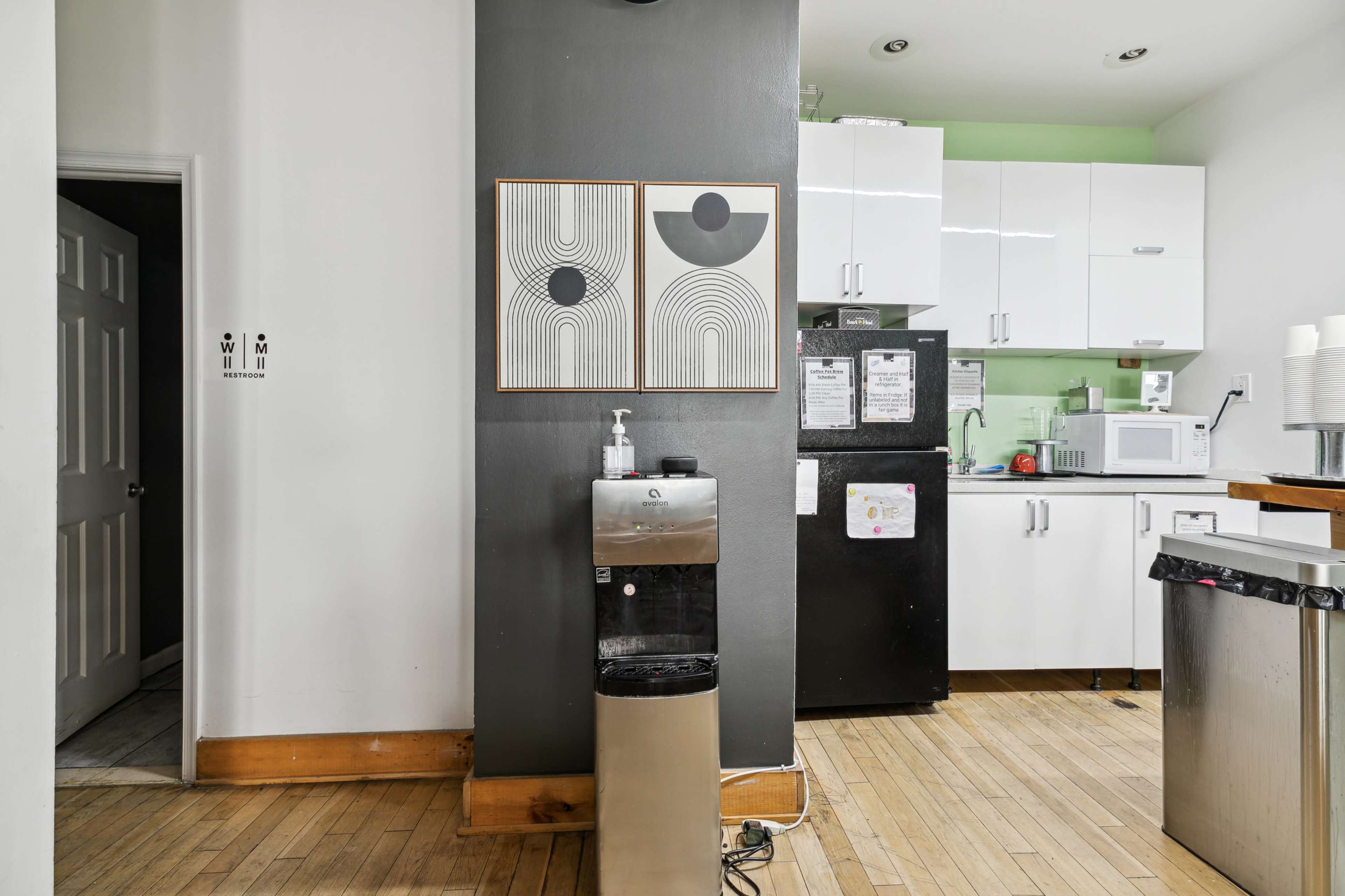 A kitchenette with a water dispenser, modern appliances, and two framed artworks on the wall.