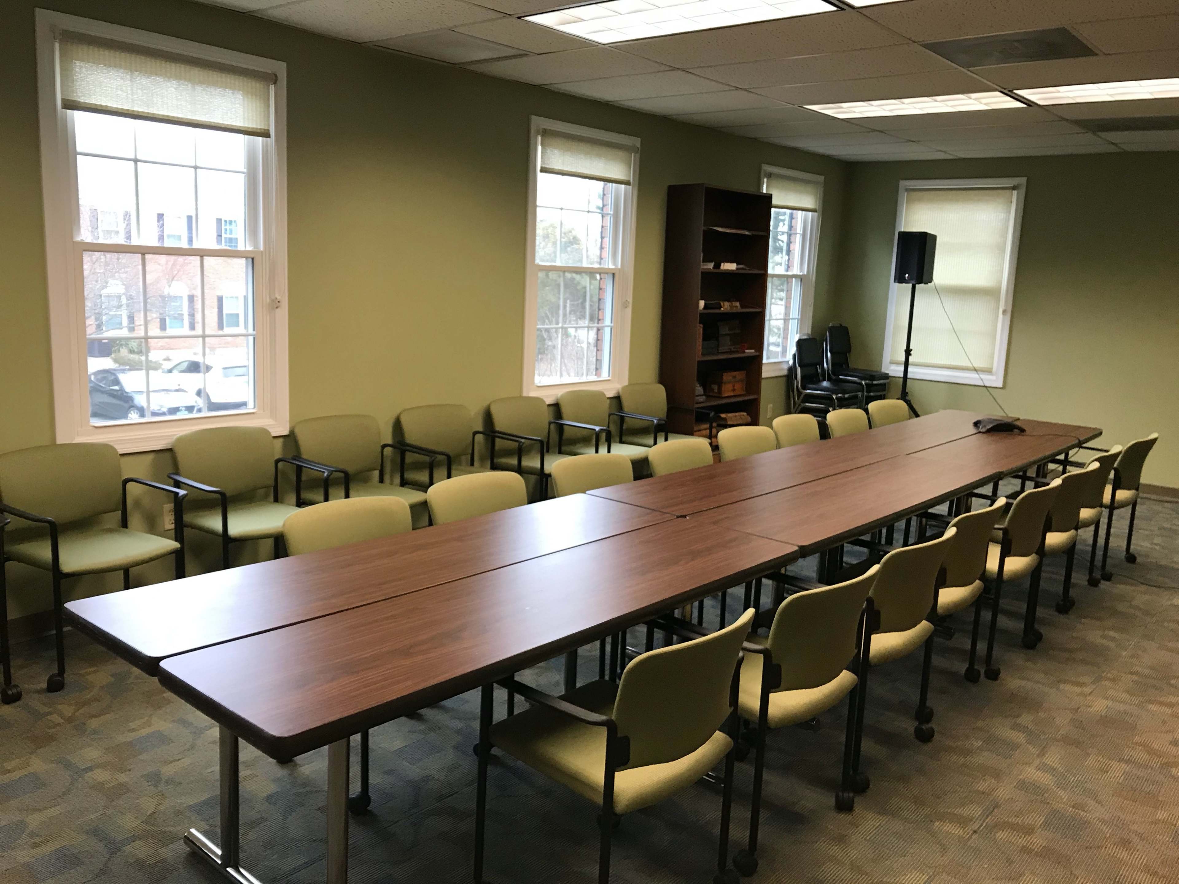 A conference room with a long wooden table surrounded by green chairs and large windows.