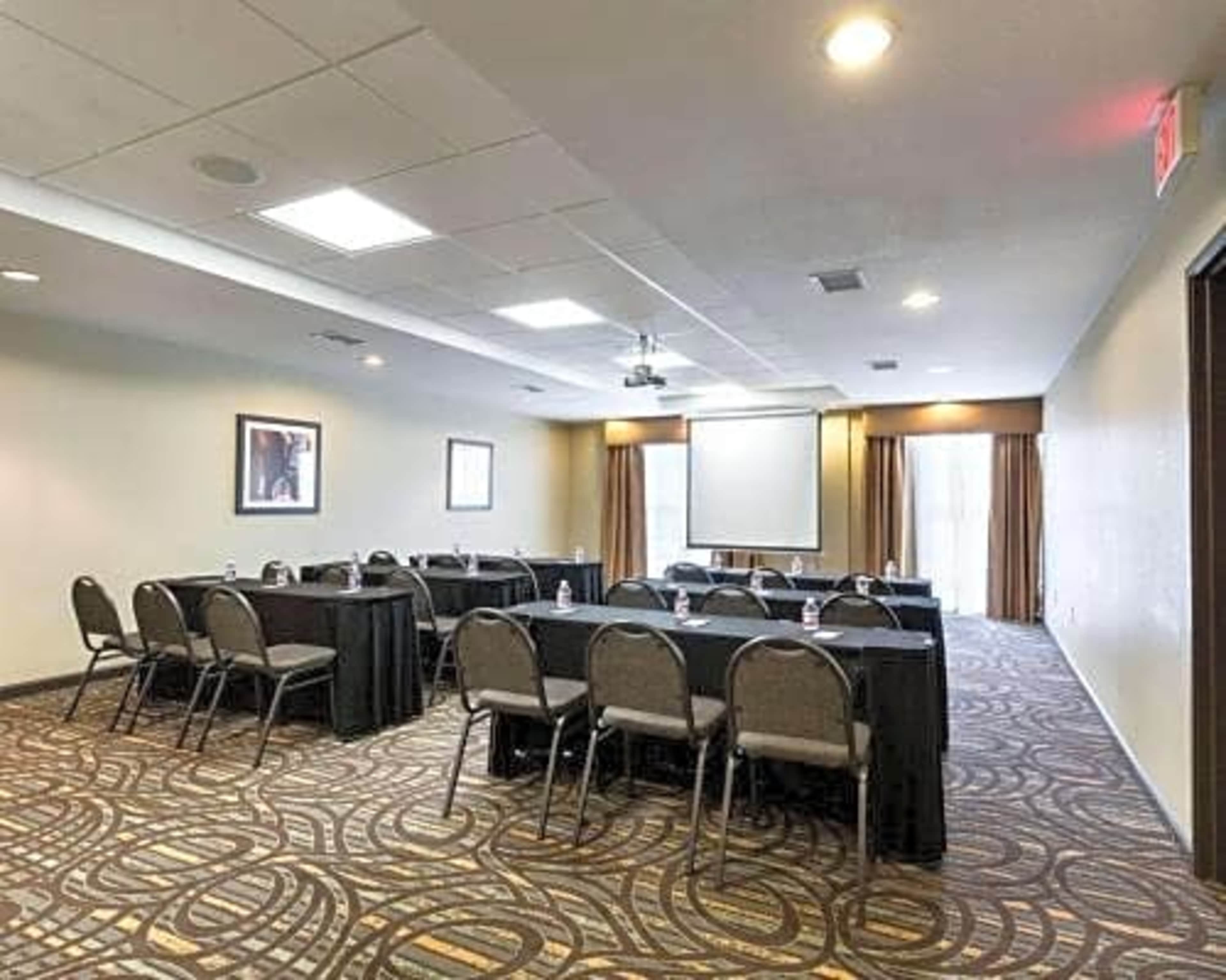 A conference room set up with multiple tables arranged in a U-shape, equipped with chairs and a projection screen at the front.