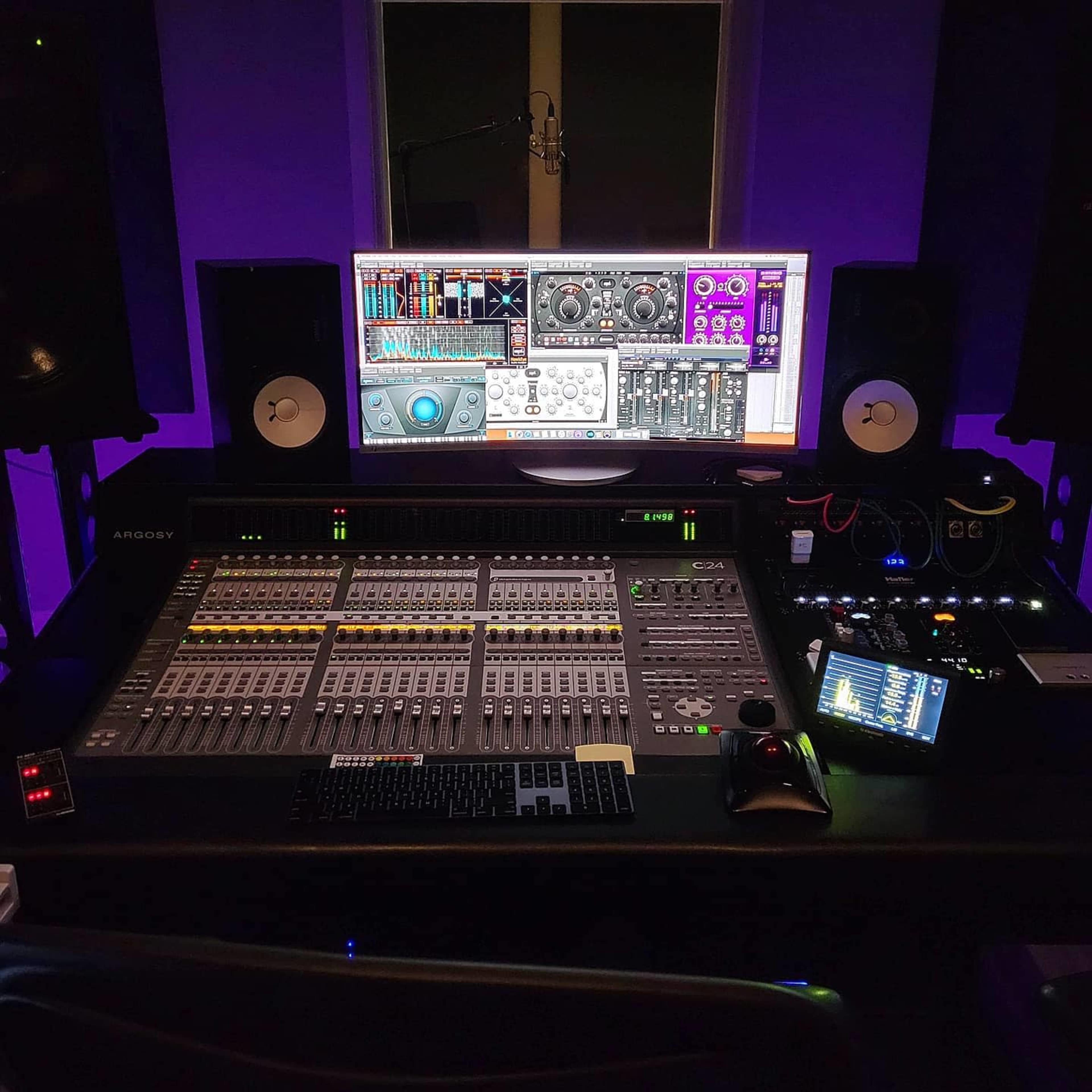 A digital audio workstation featuring a mixing console, computer monitor displaying sound editing software, and studio monitors, all set in a dimly lit environment.