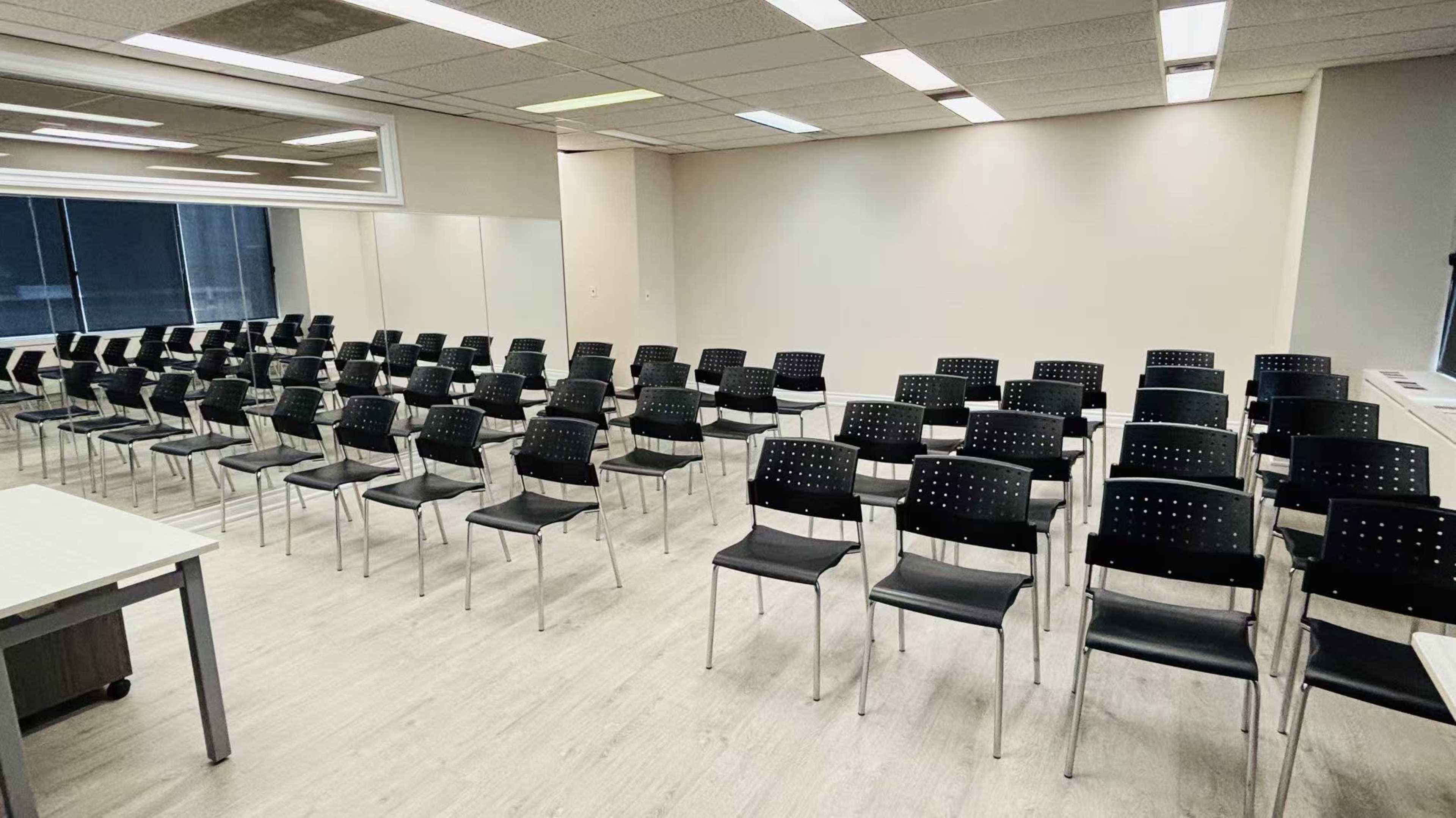 The image shows a tidy seminar room arranged with rows of black chairs facing a blank wall.