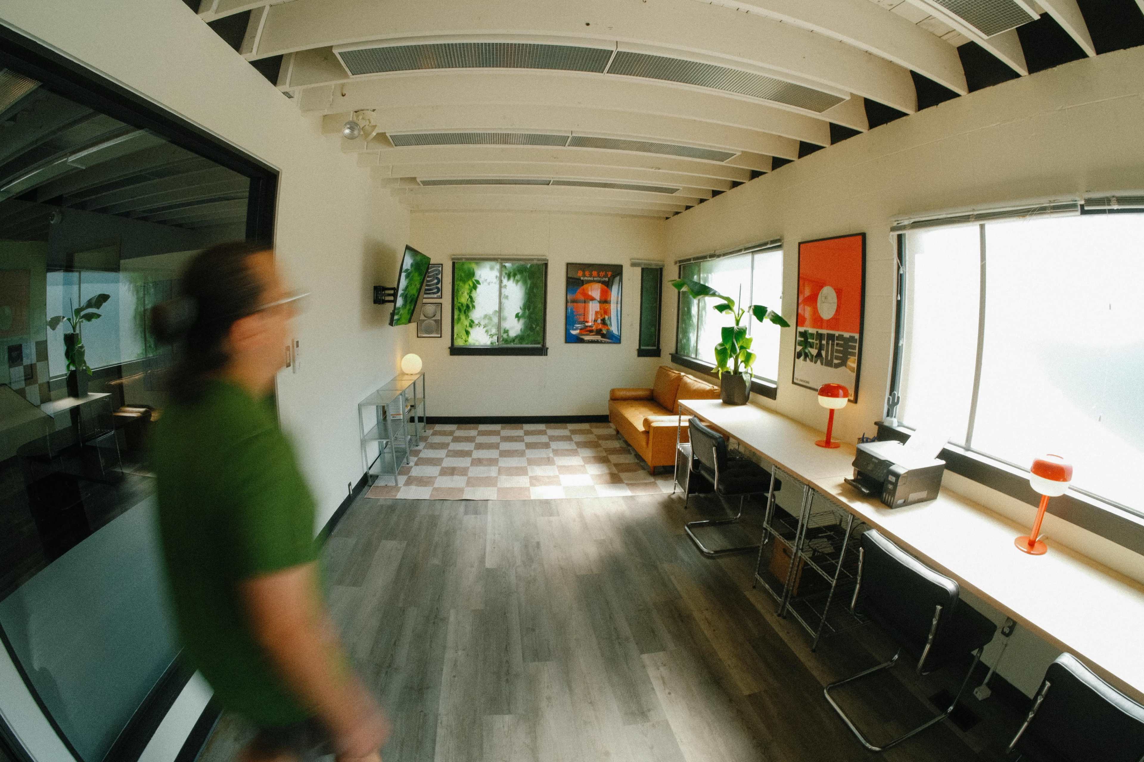 A person is walking through a modern office space featuring wooden beams, large windows, and a mix of decorative posters and plants.