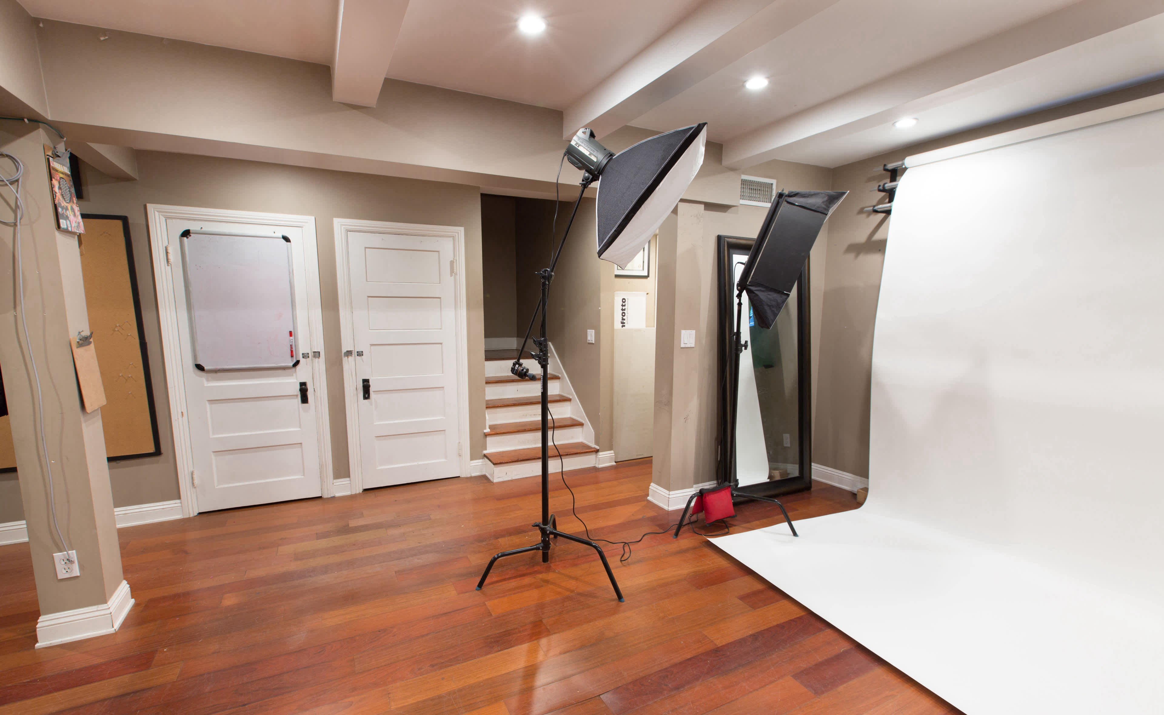 A photography studio with a white backdrop, two studio lights on stands, and wooden flooring.