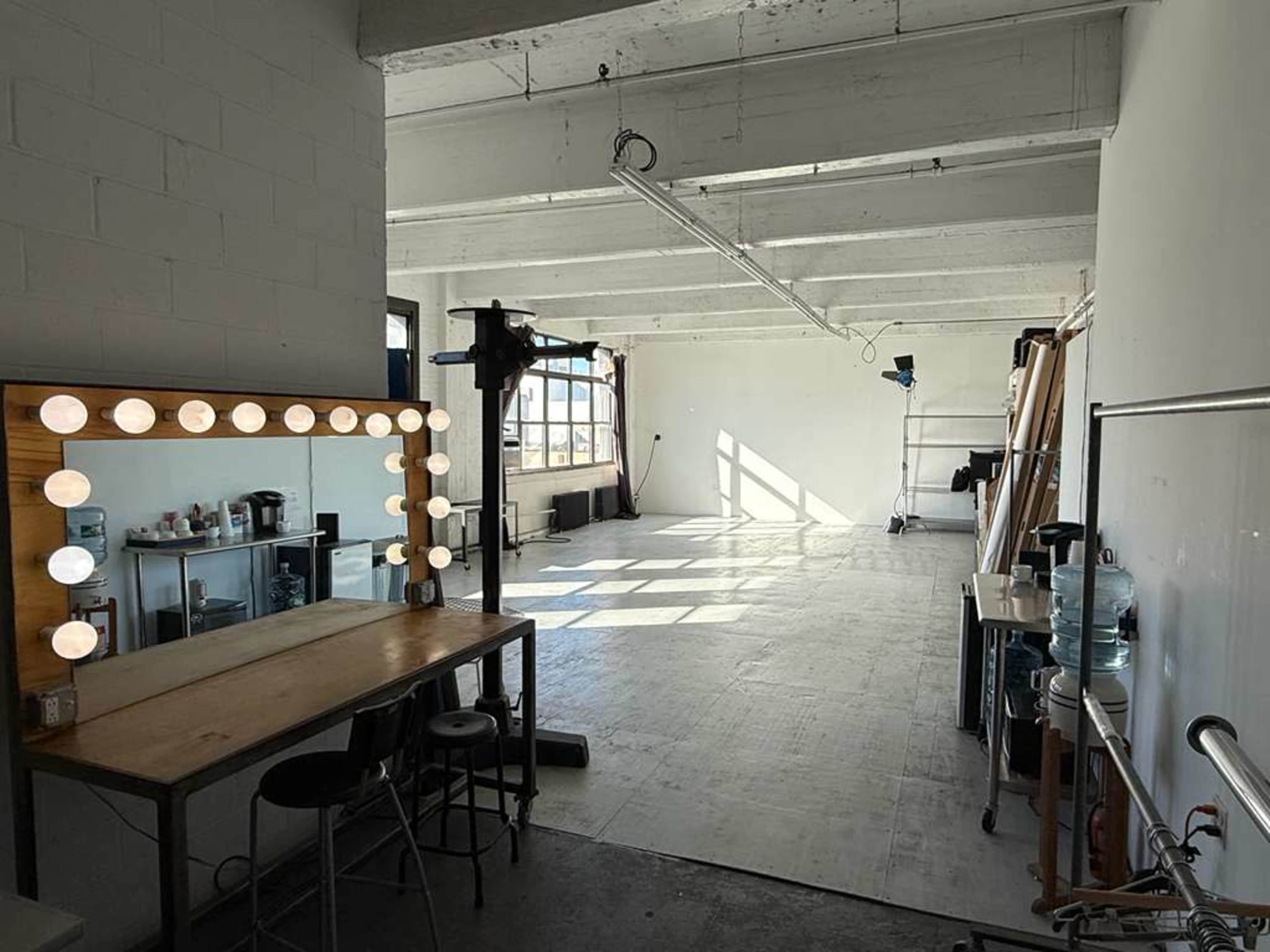 The image shows a spacious, well-lit studio with a makeup vanity, chairs, and various props arranged along one wall.