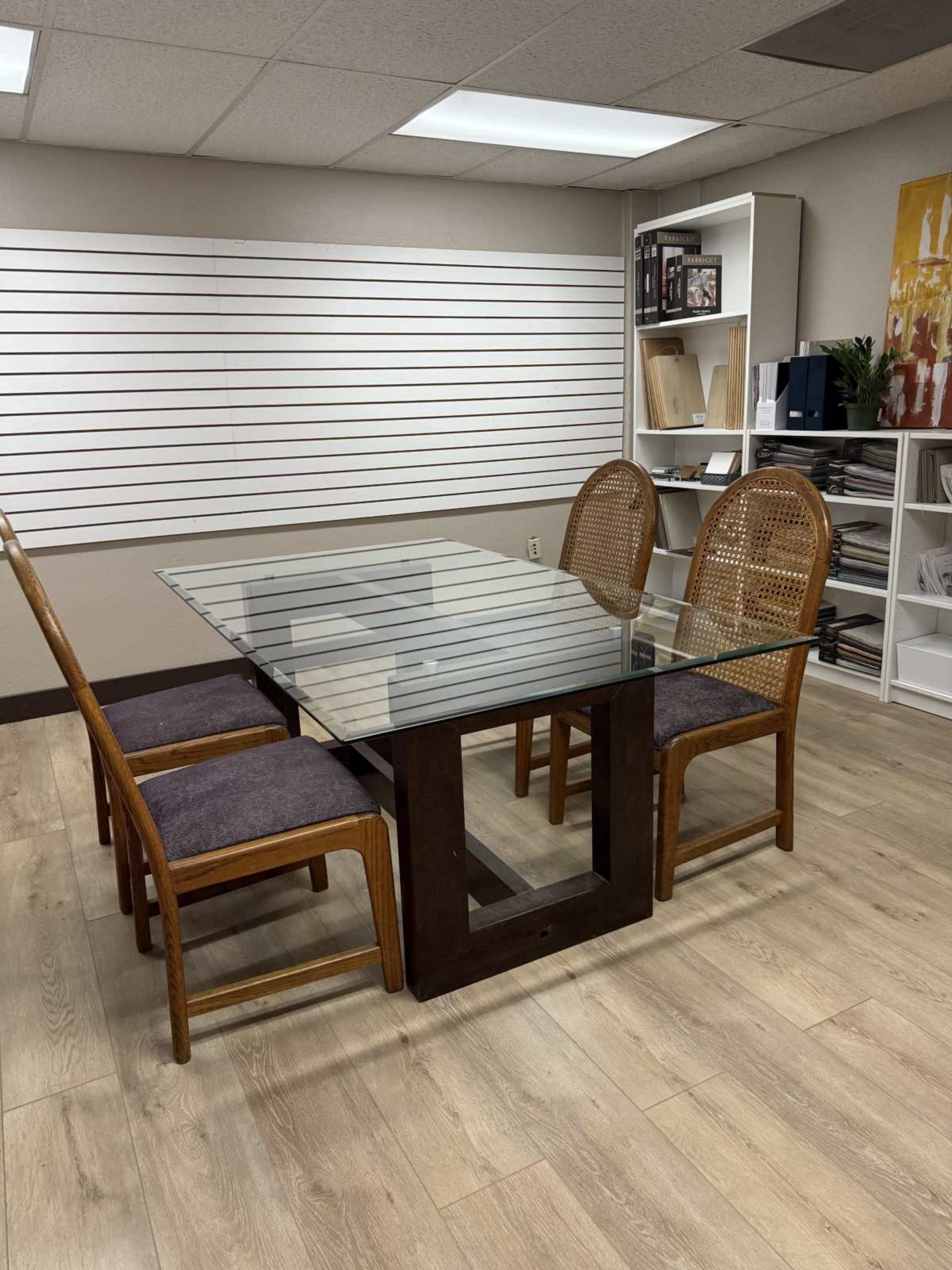 A glass-topped table with four chairs is set in a room featuring shelving and wooden flooring.