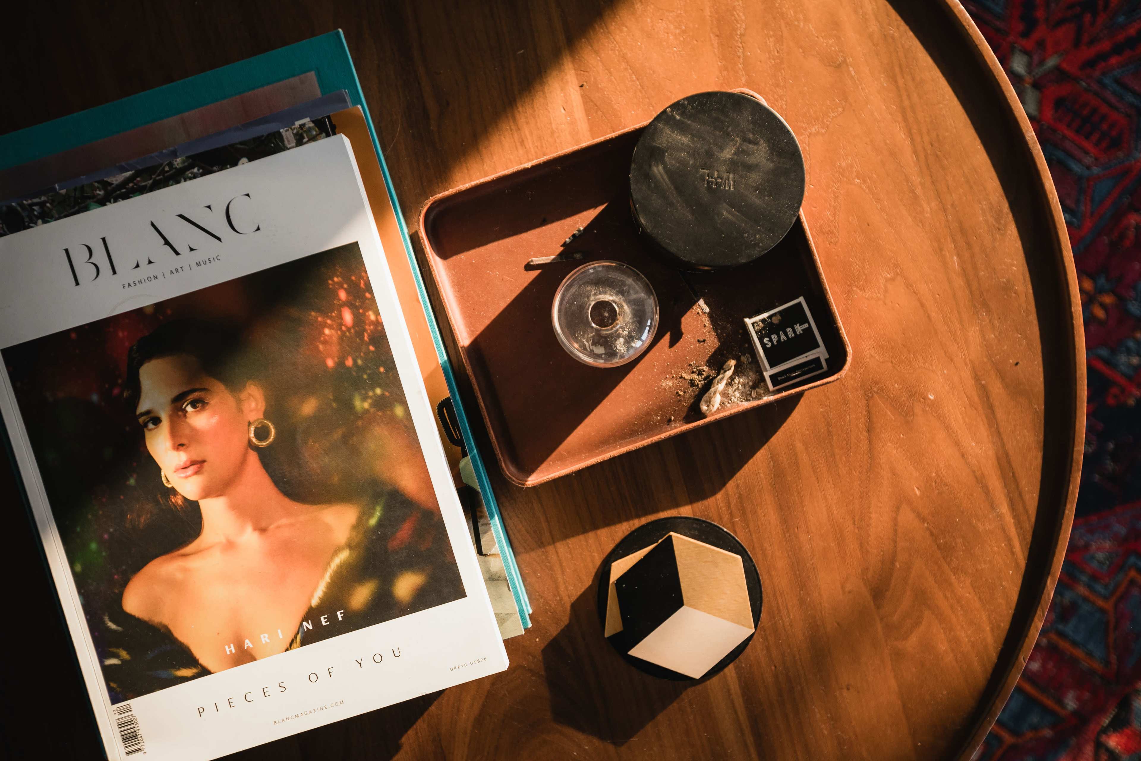 A wooden table features a fashion magazine titled "BLANC," a small dish with remnants, and a geometric decorative item.