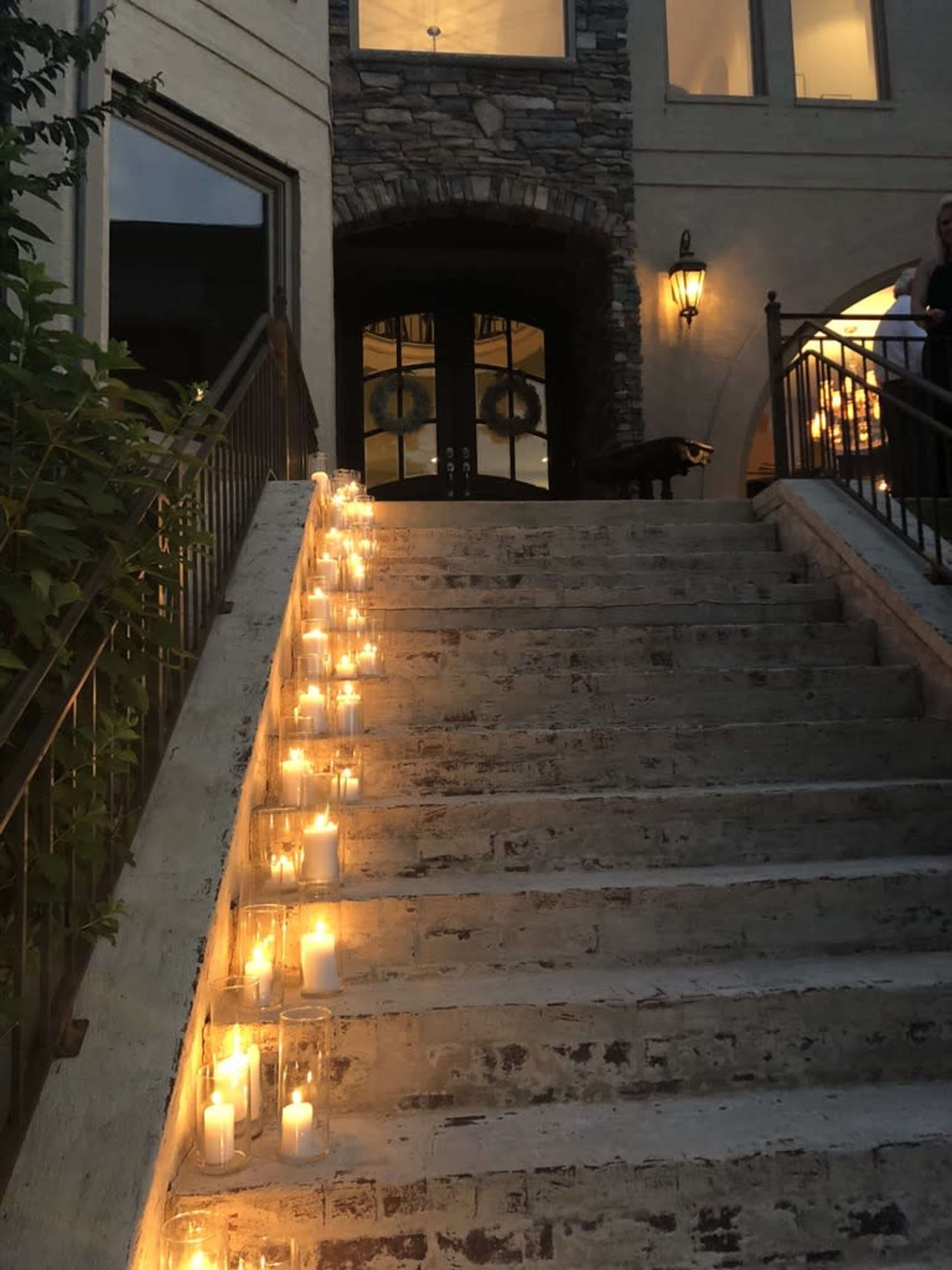 Rows of lit candles line the steps leading to a stone-faced entrance with large double doors.
