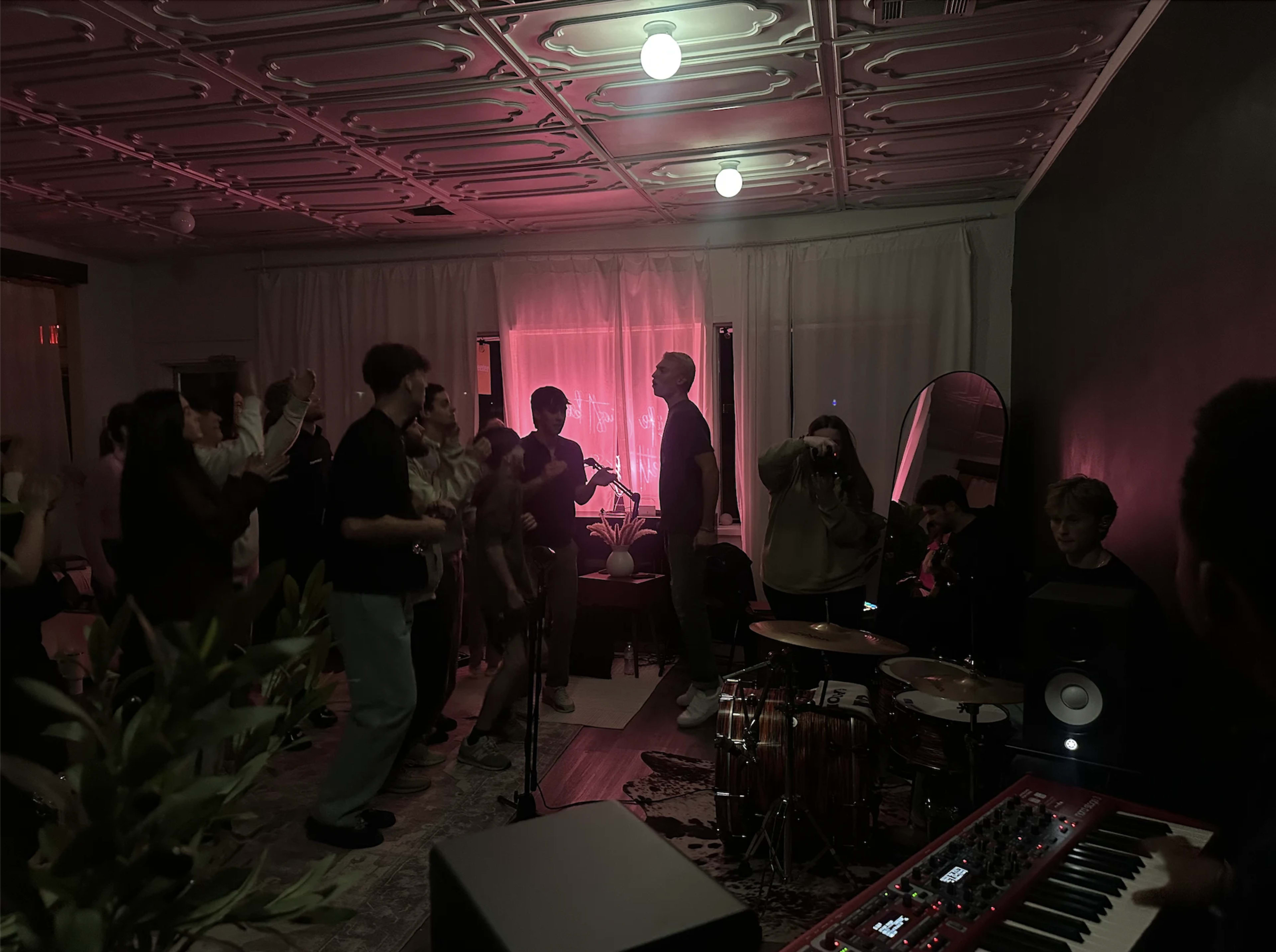 A group of people are gathered in a dimly lit room, dancing and enjoying music while a band plays in the corner.