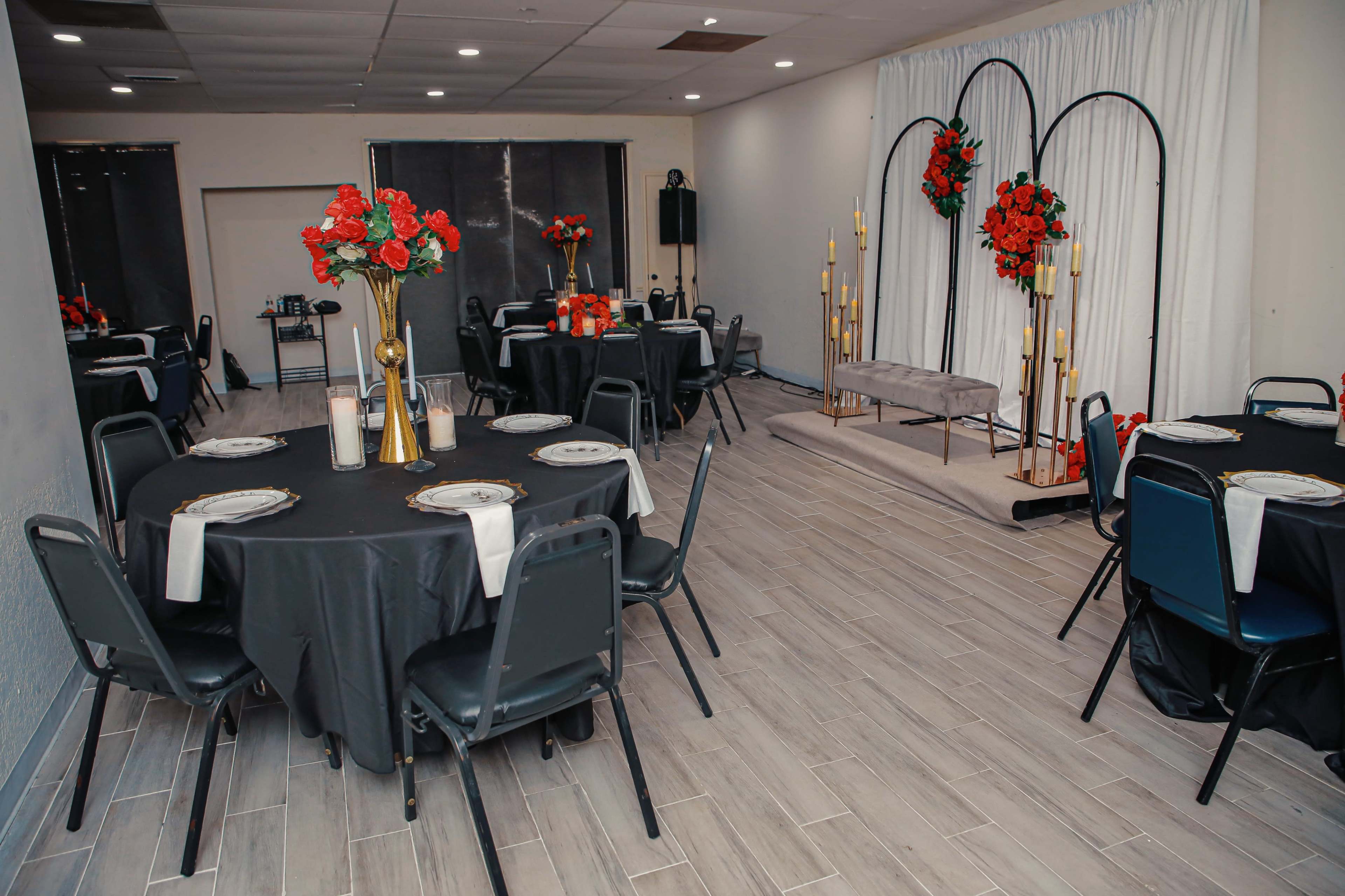 A banquet hall with black tables set for an event, featuring floral centerpieces and a backdrop of candles and floral arrangements.