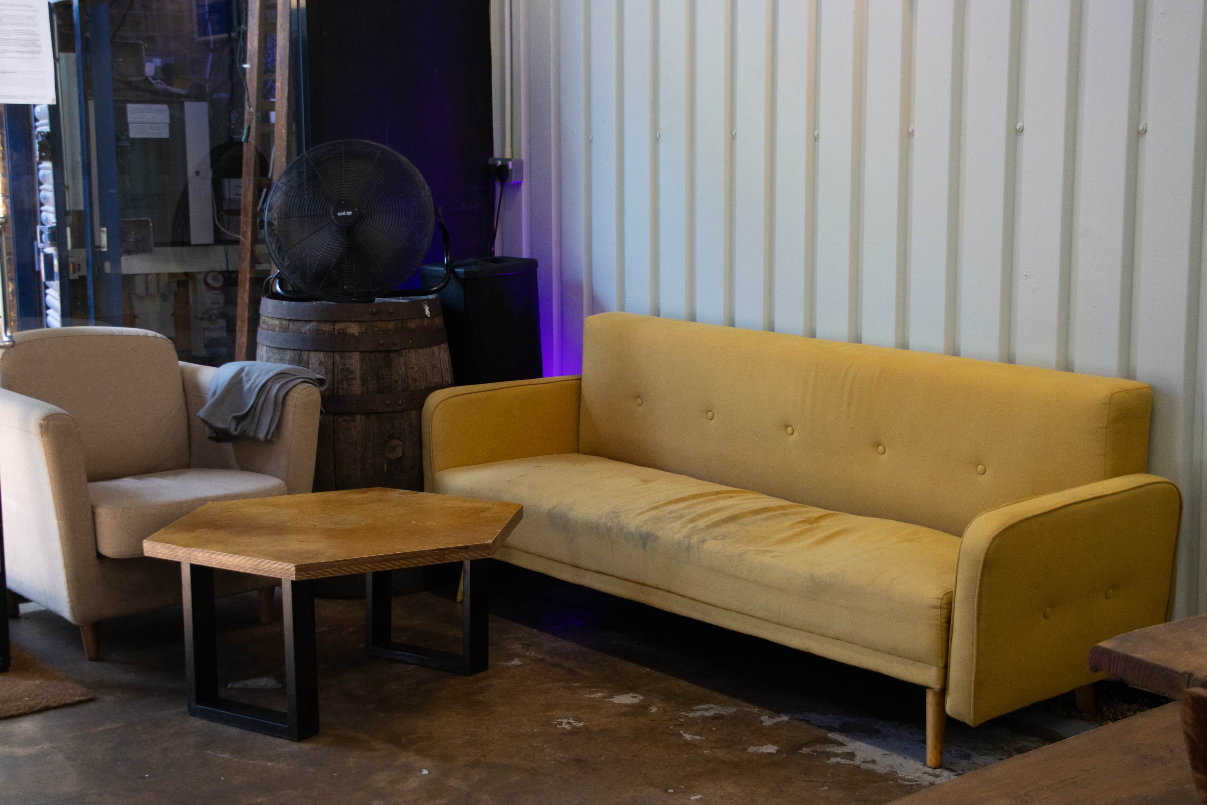 The image shows a yellow couch and a beige armchair next to a wooden hexagonal coffee table in a cozy indoor setting.