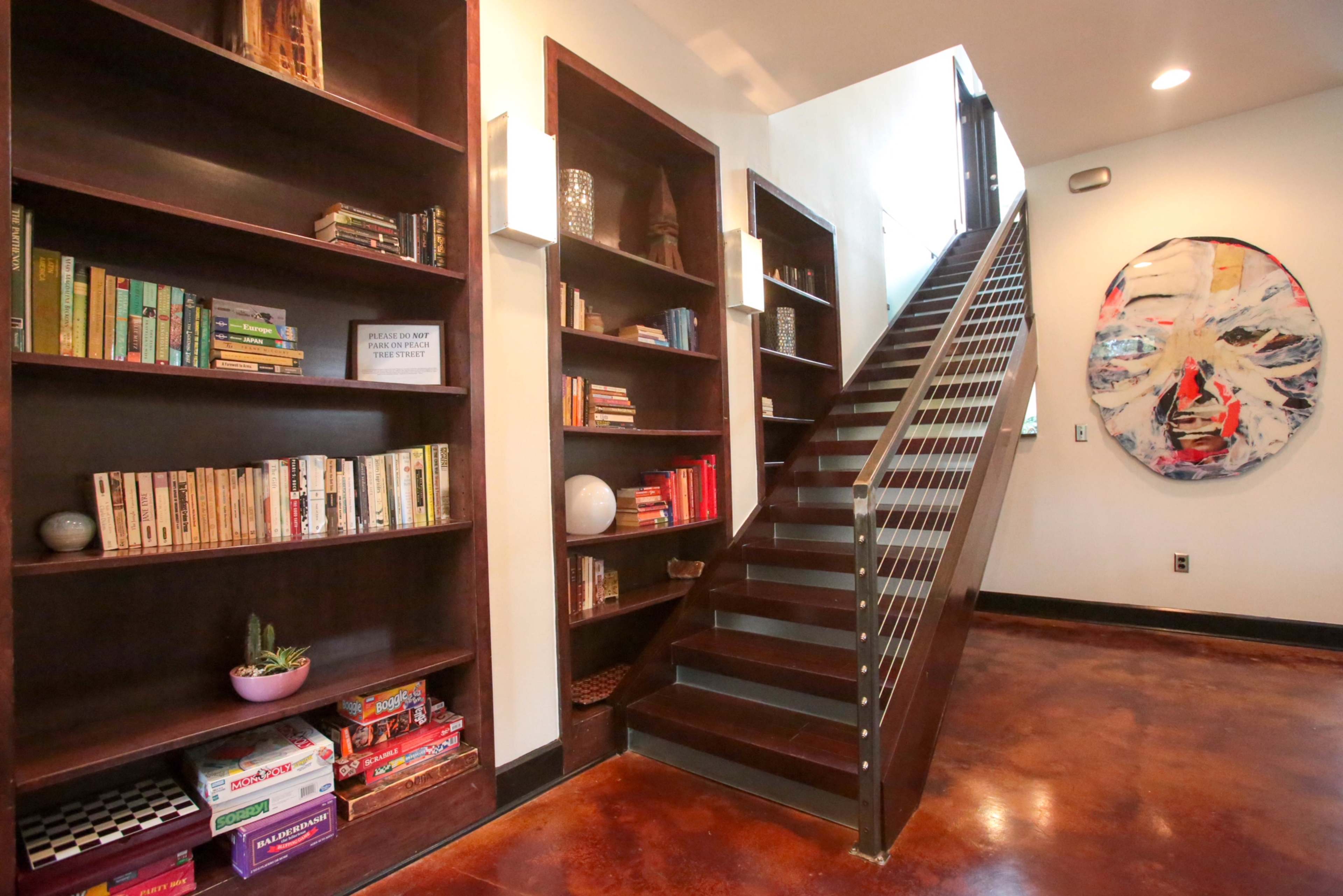 A modern hallway featuring built-in bookshelves filled with books, a plant, and a staircase leading to an upper level.