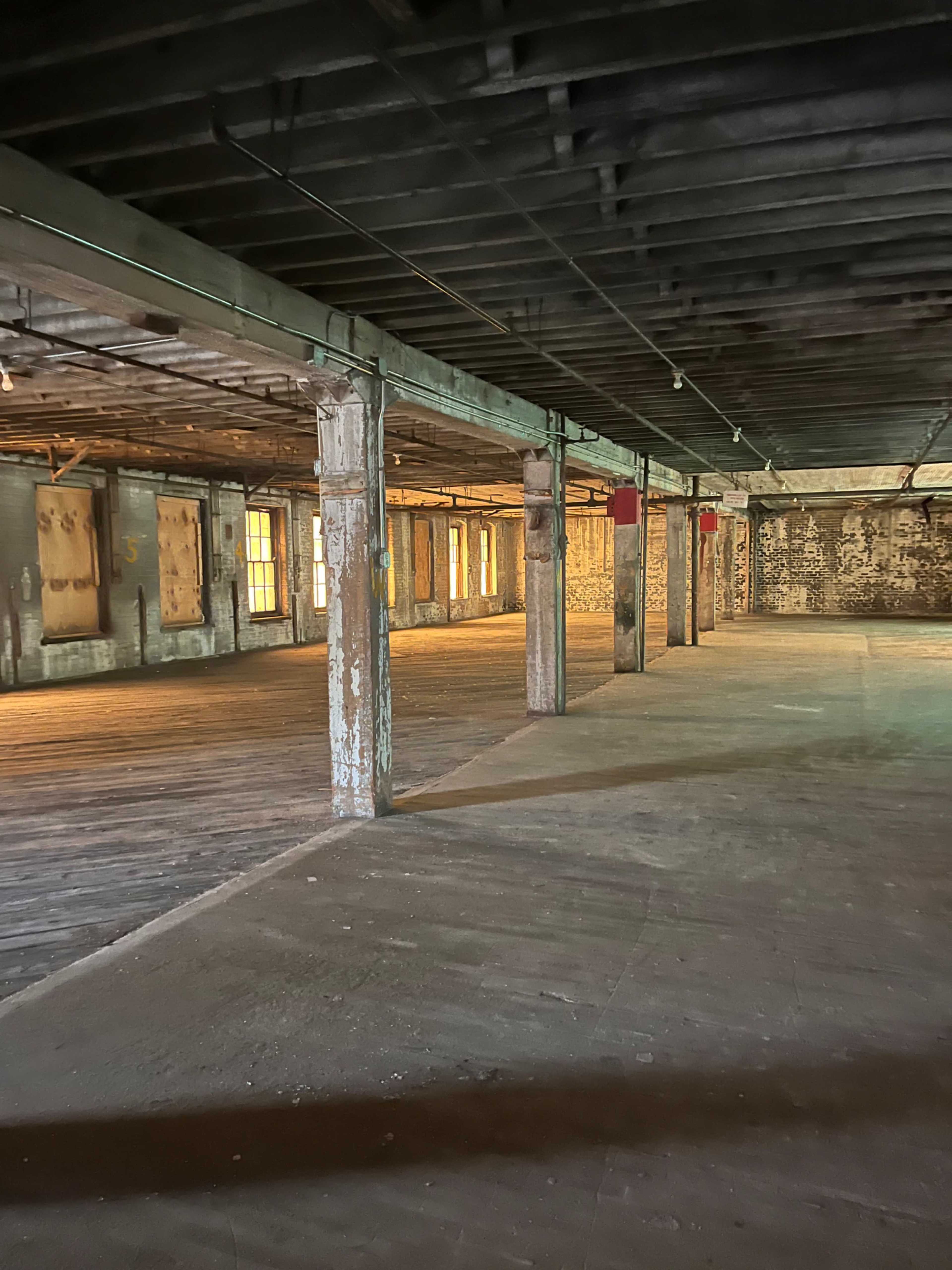 The image shows an empty, dimly lit room with wooden floors, exposed beams, and weathered walls.