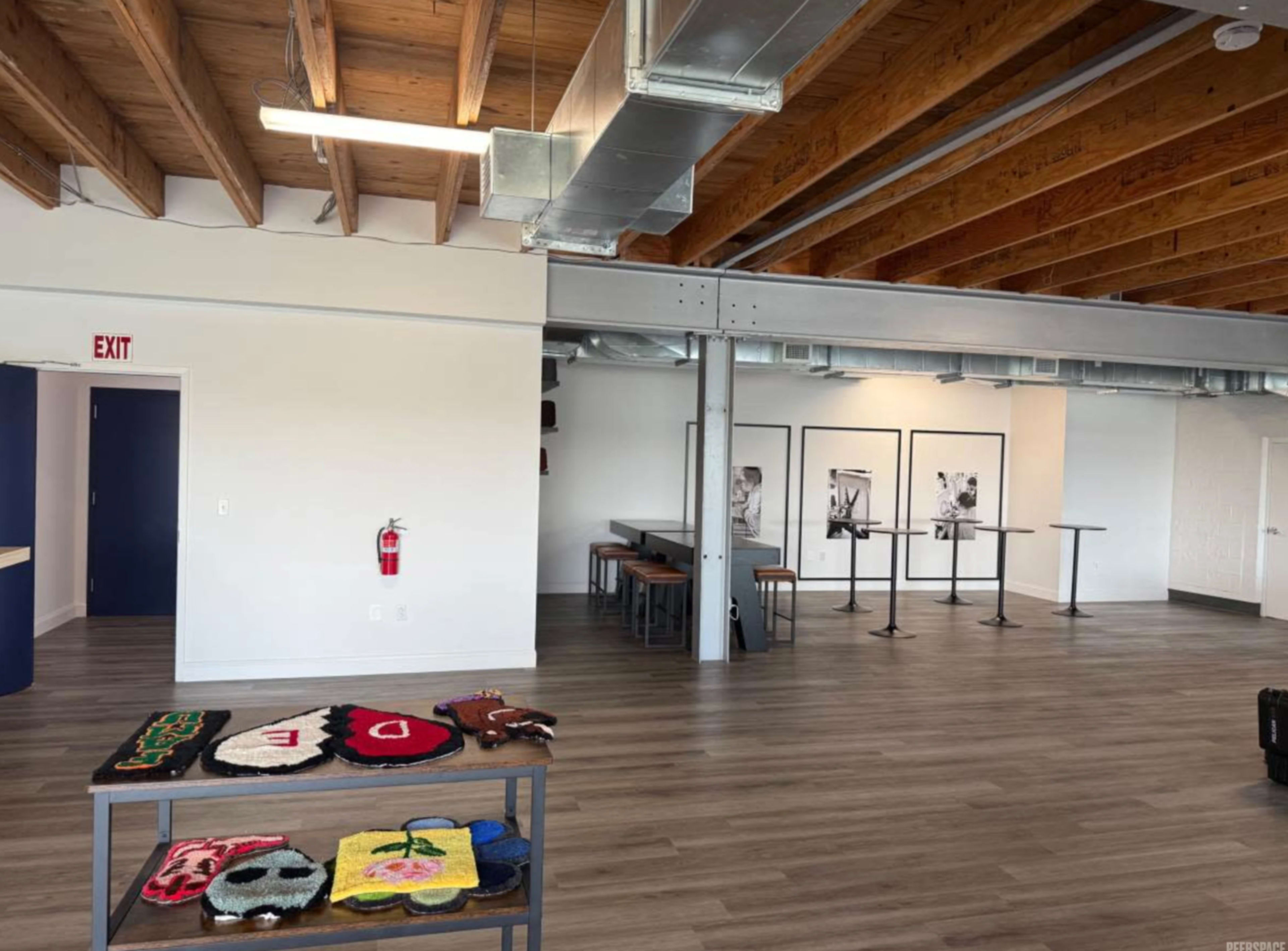 The scene shows a spacious interior with wooden beams, a display of colorful bags on a table, and several tables and chairs arranged in the area.