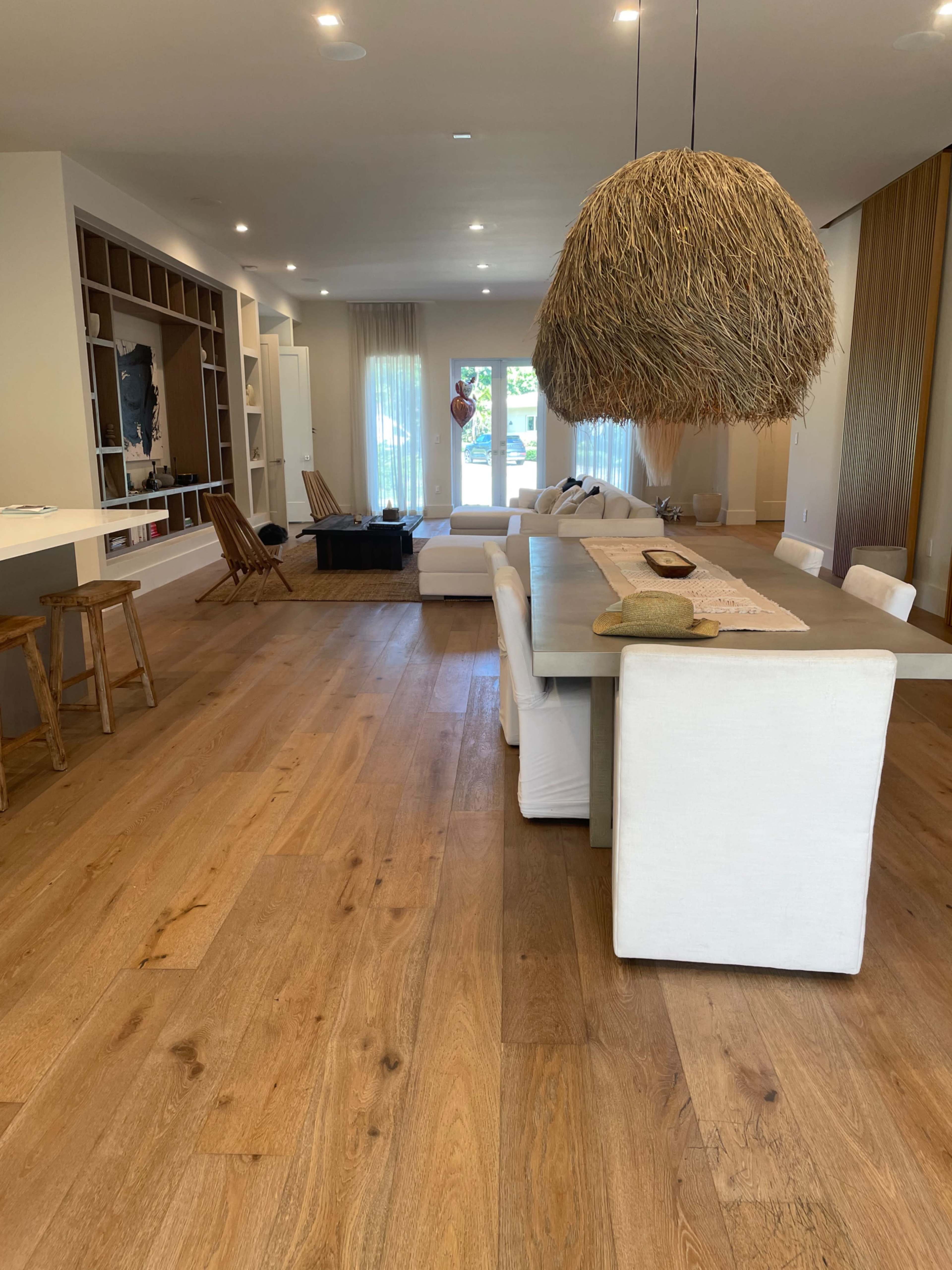 A spacious living area features a long dining table, a large white sofa, and a decorative overhead light made of natural materials.