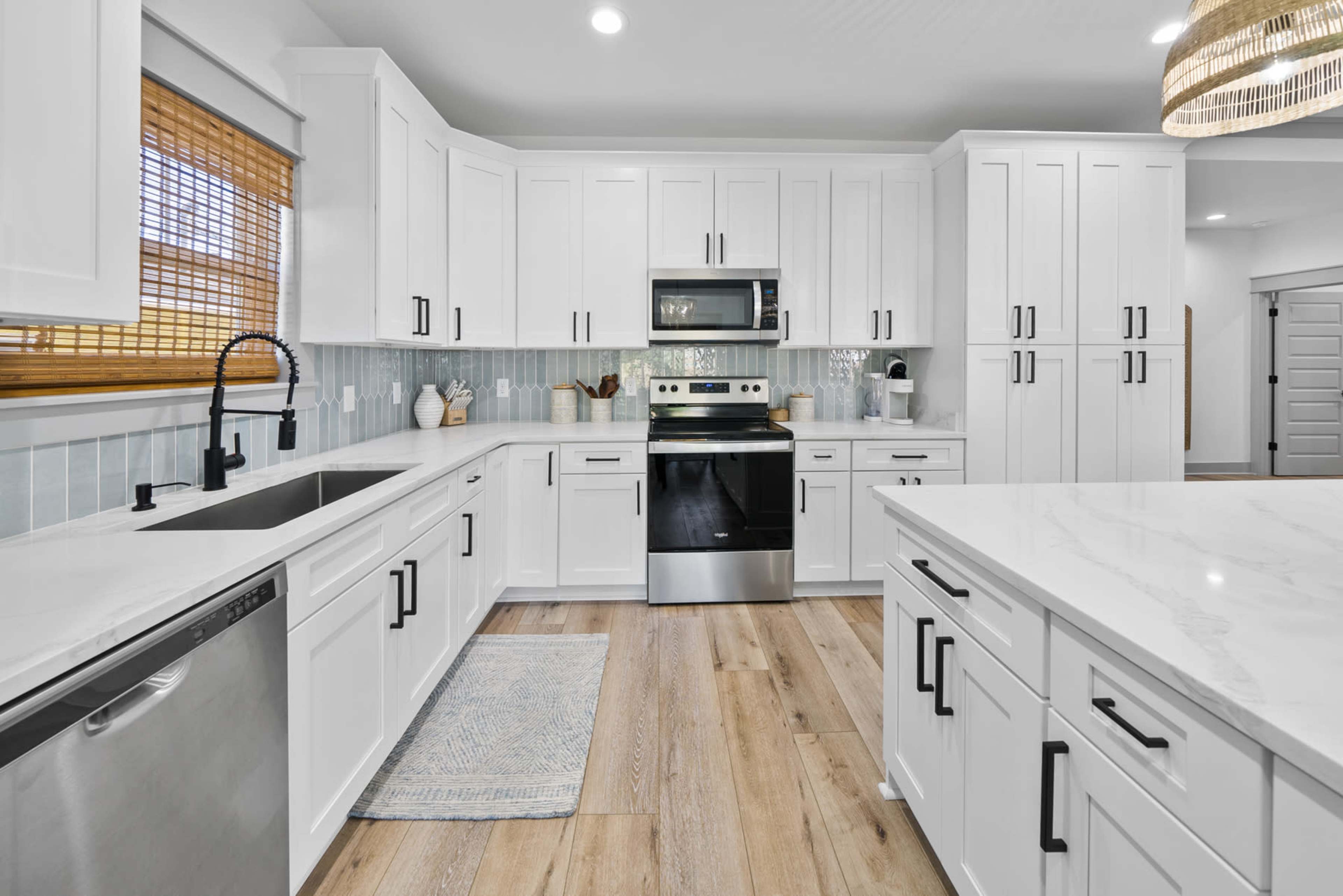 The image shows a modern kitchen with white cabinetry, stainless steel appliances, and a central island topped with marble.