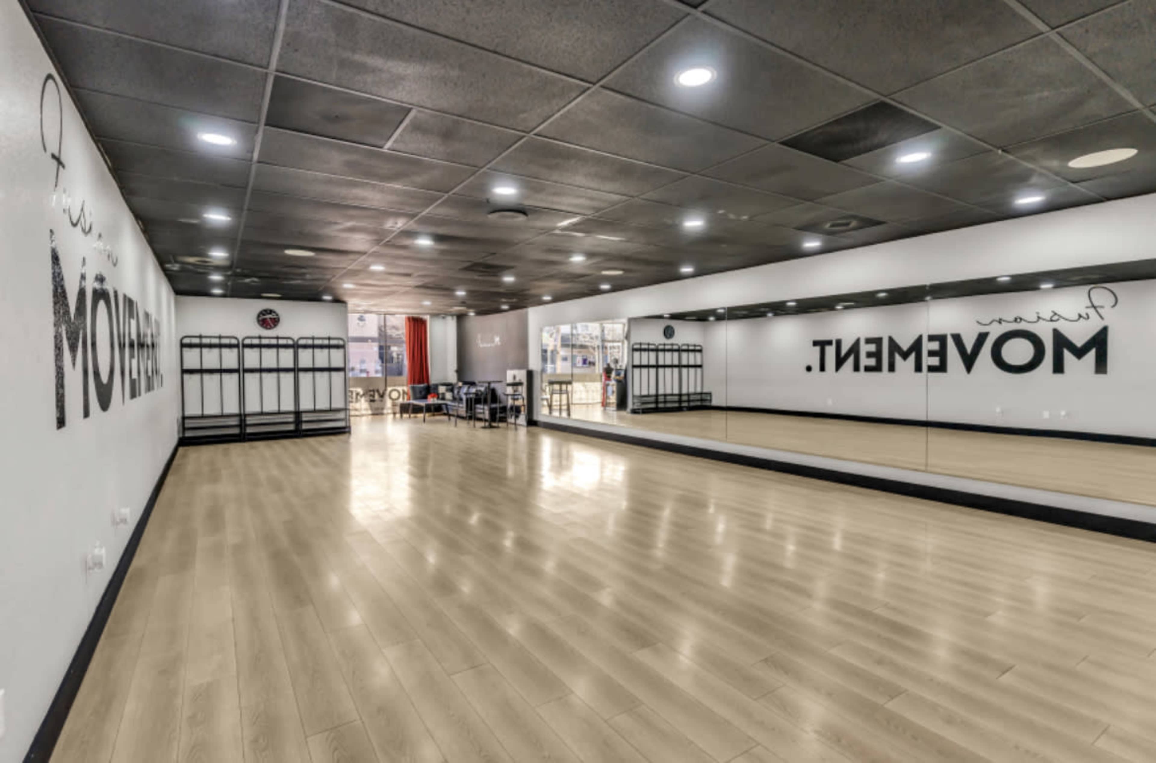 A spacious dance studio with mirrored walls and a wooden floor, featuring the word "MOVEMENT" displayed prominently on one side.