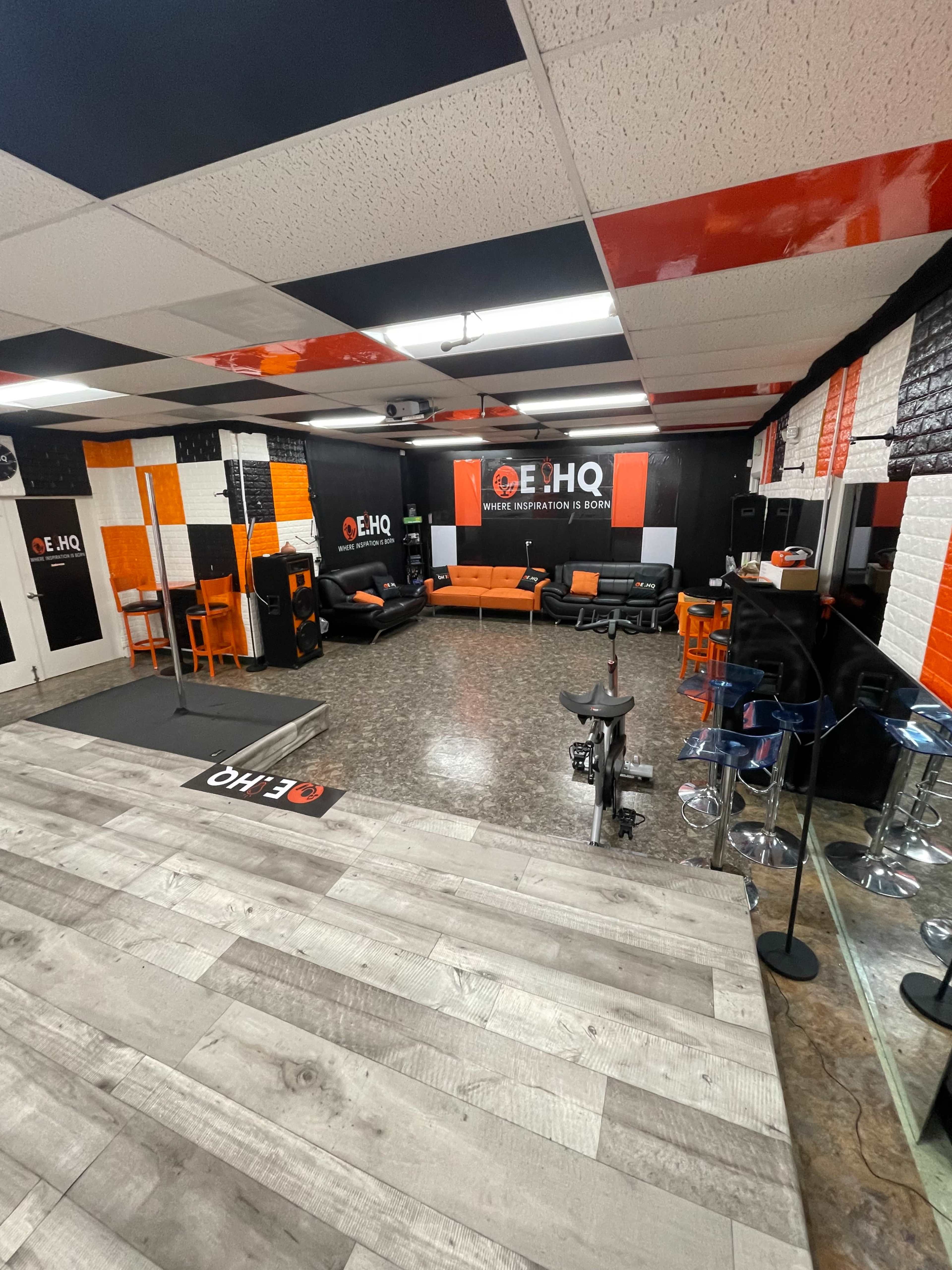 A modern lounge area with black and orange walls, featuring seating, tables, and exercise equipment.