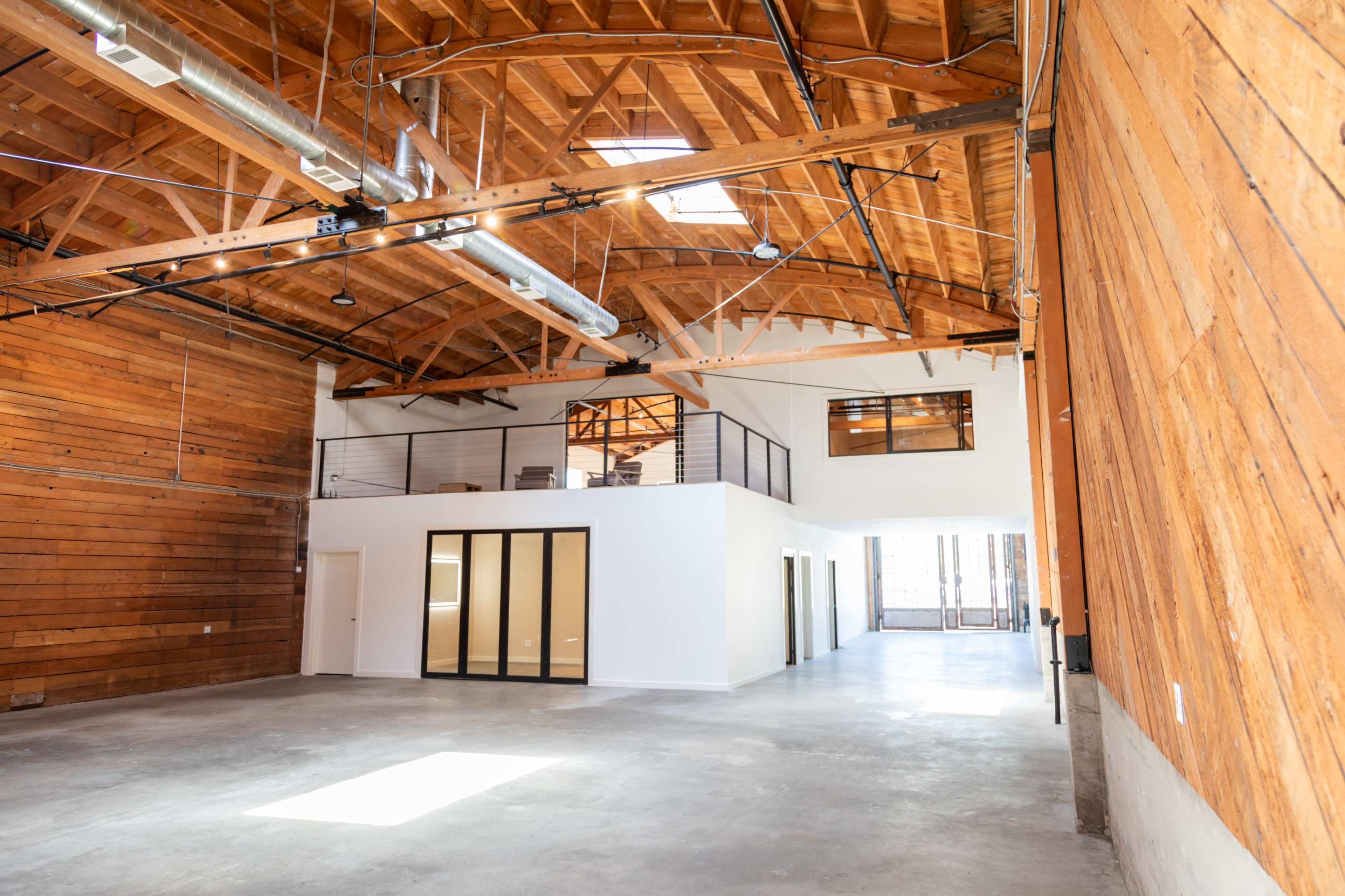 A spacious interior of a modern industrial-style building with wooden beams and a polished concrete floor.