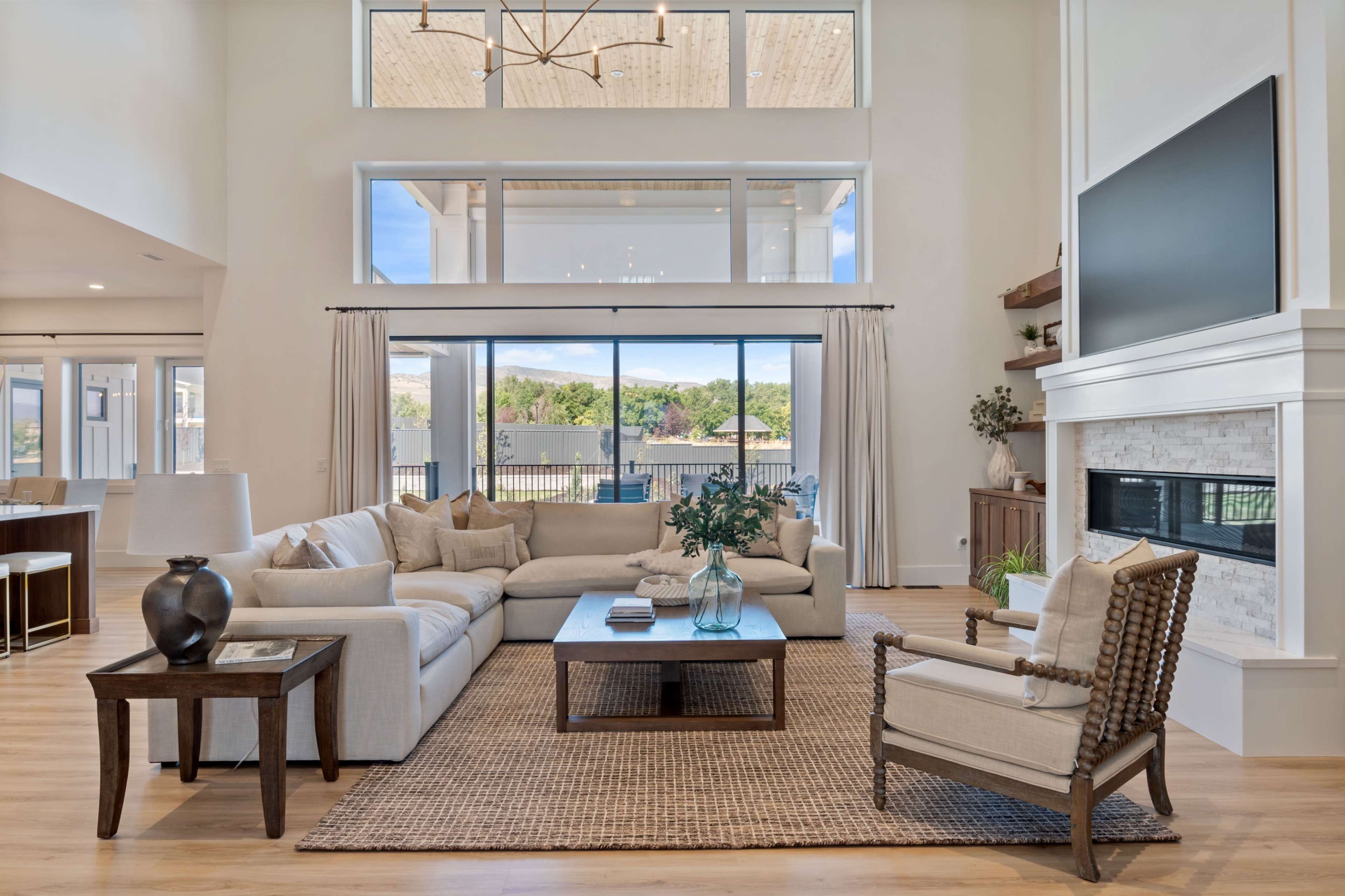 A spacious living room features a large sectional sofa, a coffee table, and a fireplace with ample natural light coming through large windows.