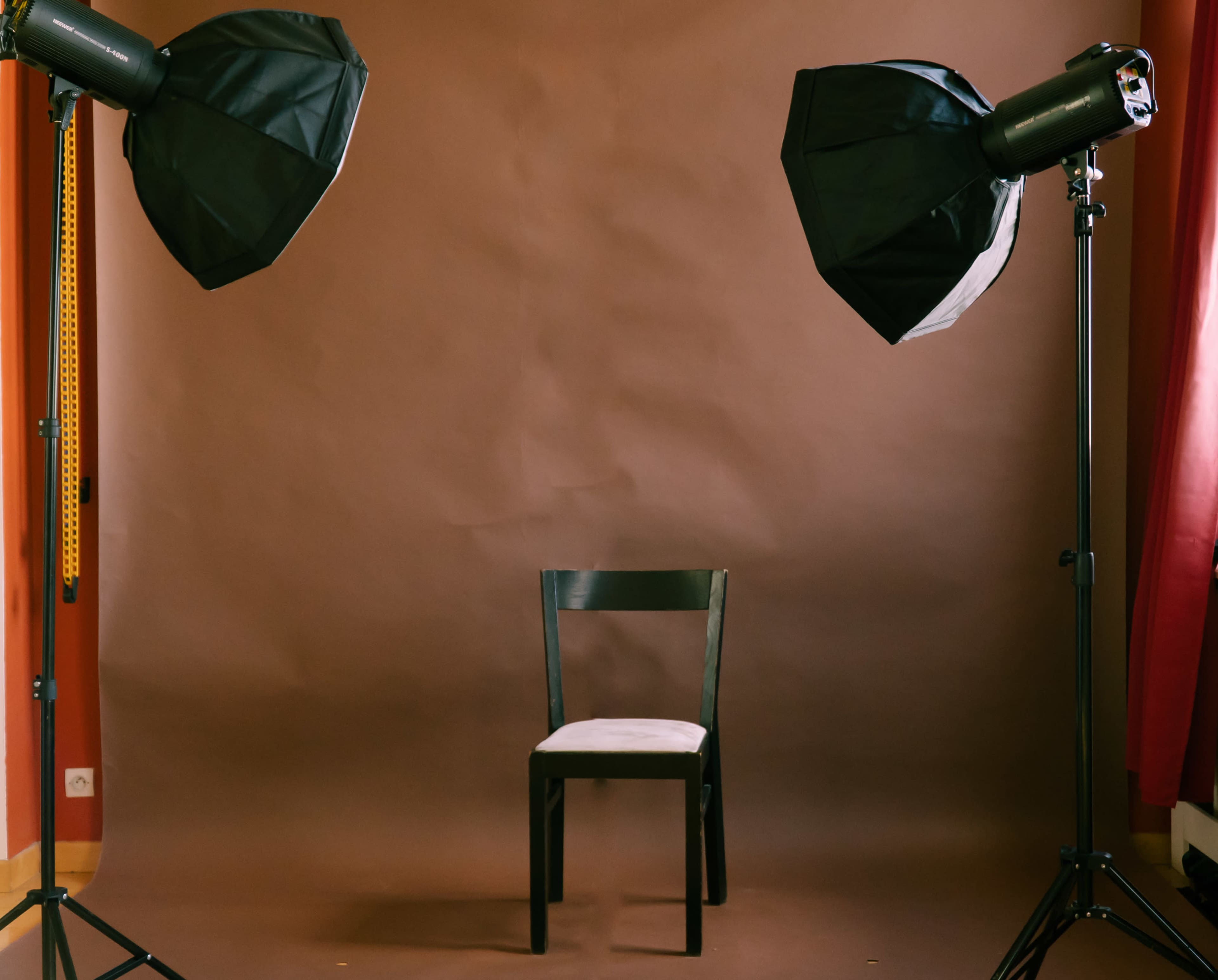 A black chair positioned in front of a brown backdrop, illuminated by two softbox lights on either side.