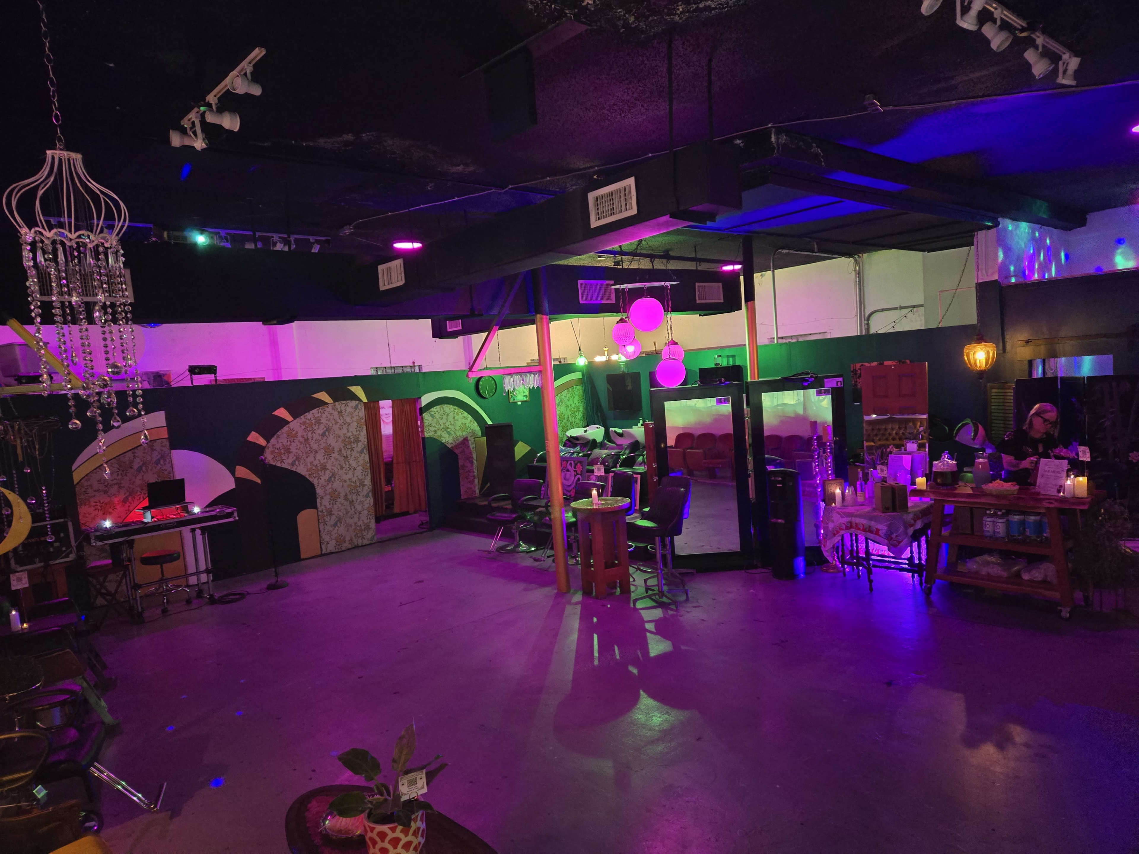 The image shows a spacious room with colorful lighting, featuring various salon stations and decorative elements.