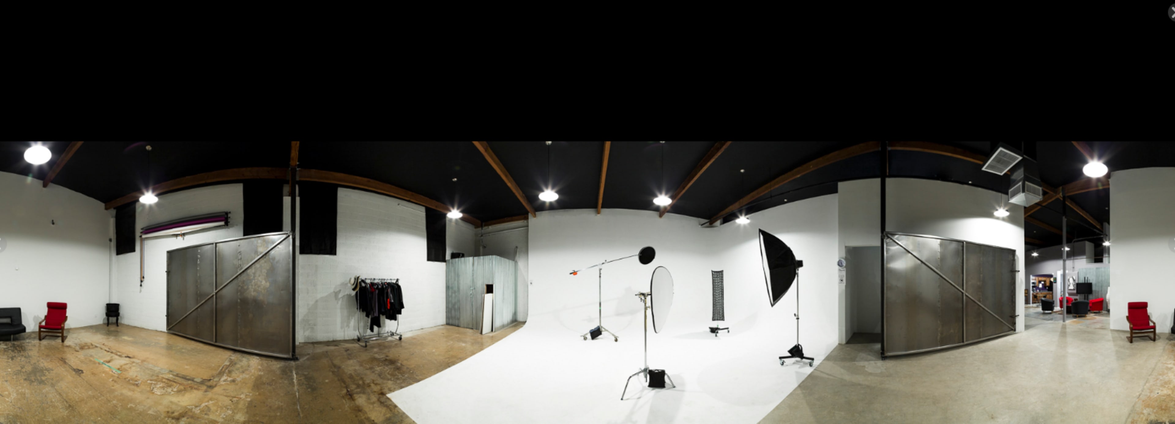 The image shows a spacious photography studio featuring a white backdrop, lighting equipment, and a rack with clothing against a stark industrial interior.