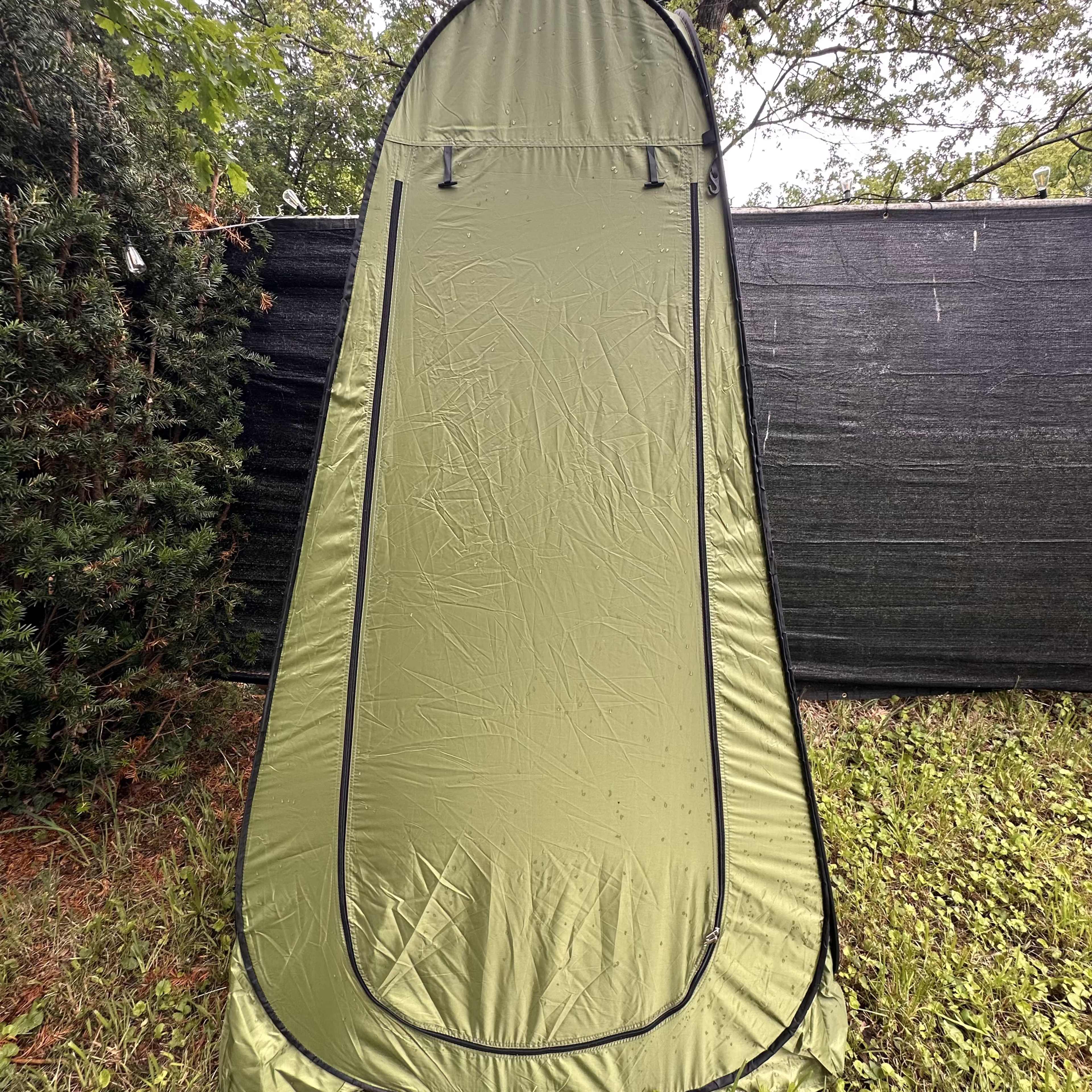 A green pop-up tent is set up on grass near a black backdrop.