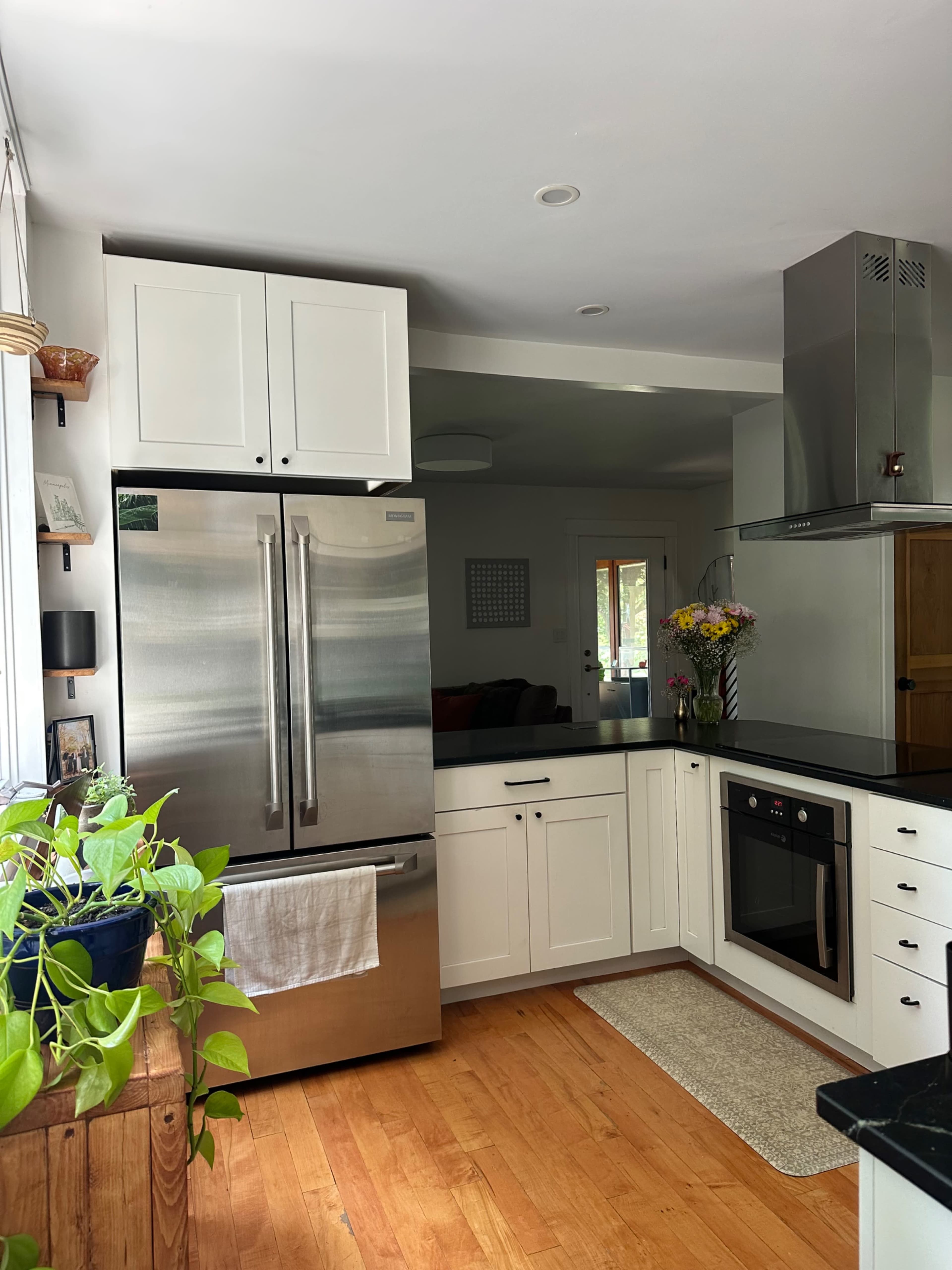 The image shows a modern kitchen with white cabinetry, stainless steel appliances, and a wooden floor.