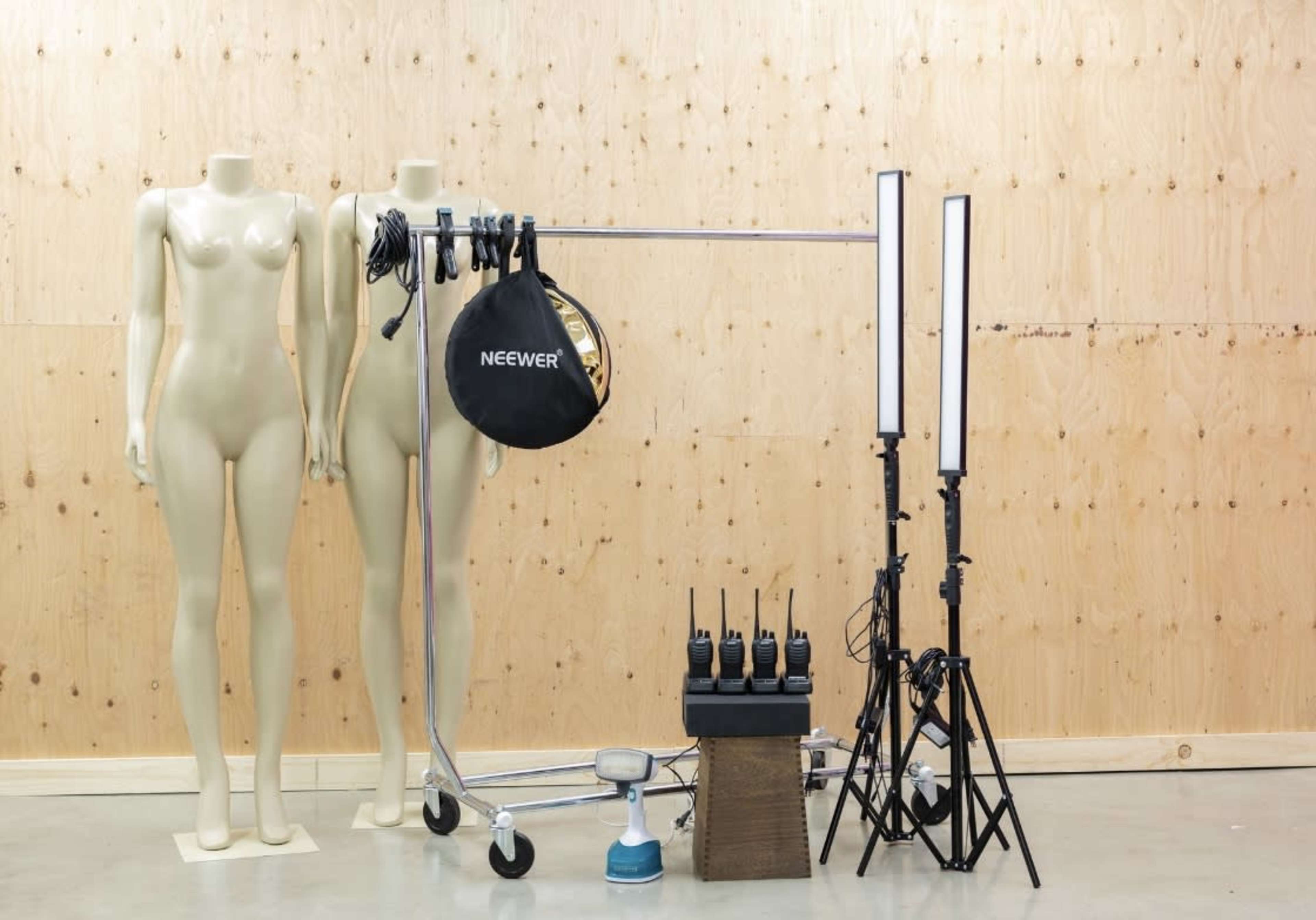 The image shows two mannequins alongside a clothing rack with lighting equipment and wireless communication devices set up against a wooden background.