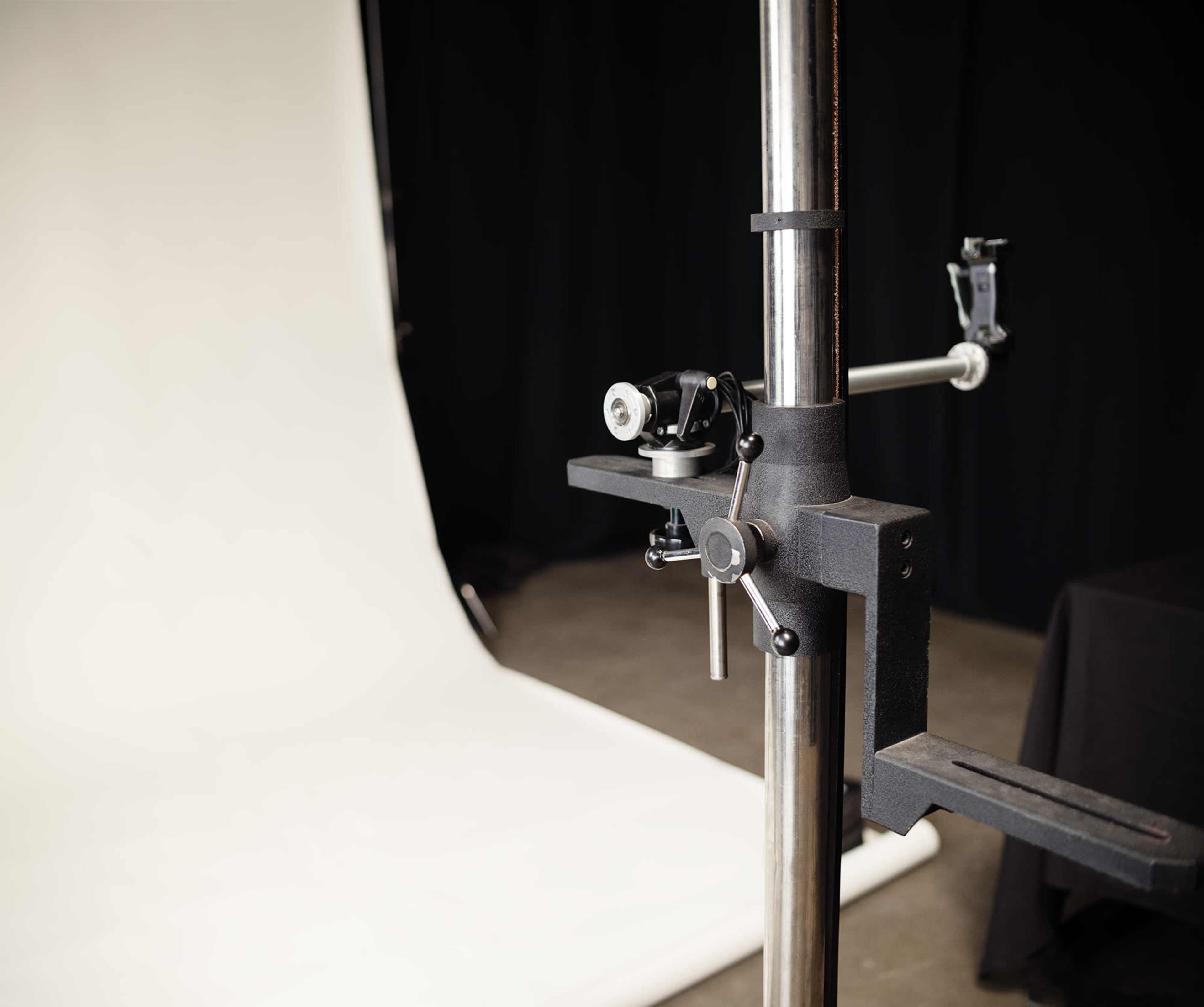 A metal photography backdrop stand is positioned next to a plain white backdrop in a studio setting.
