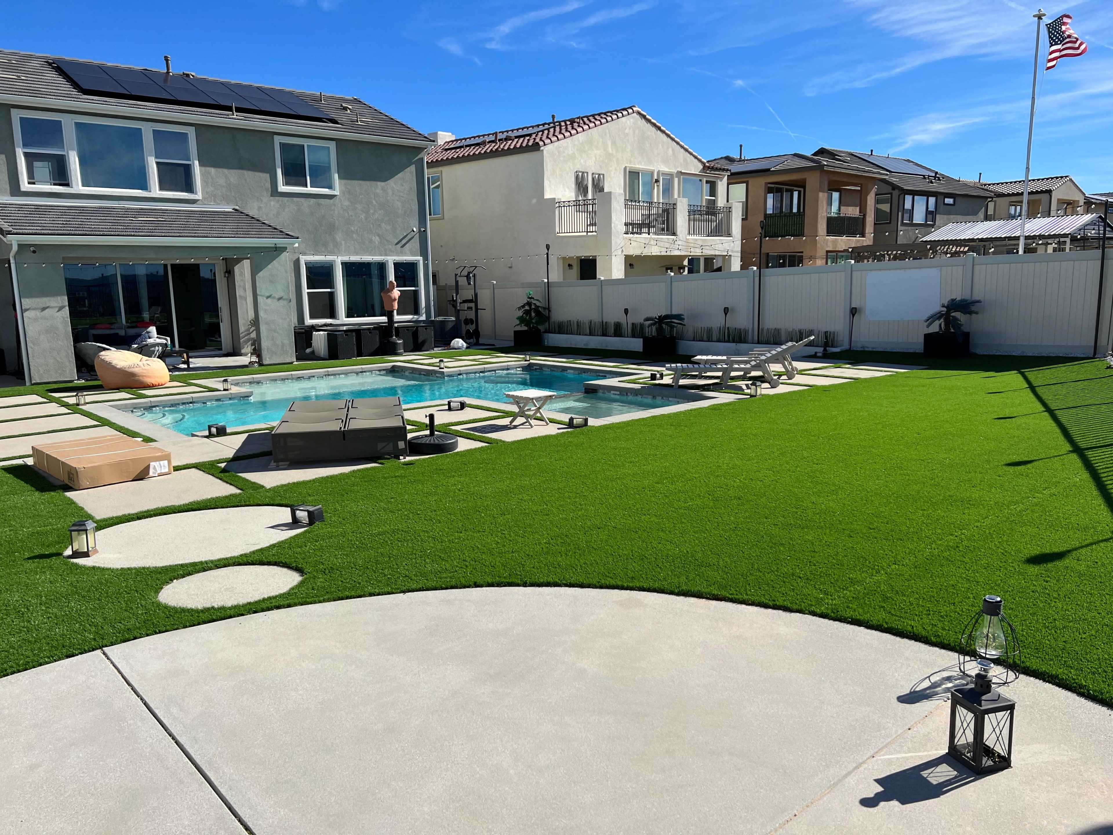 The image shows a backyard with a swimming pool surrounded by patio furniture, artificial grass, and a house in the background.