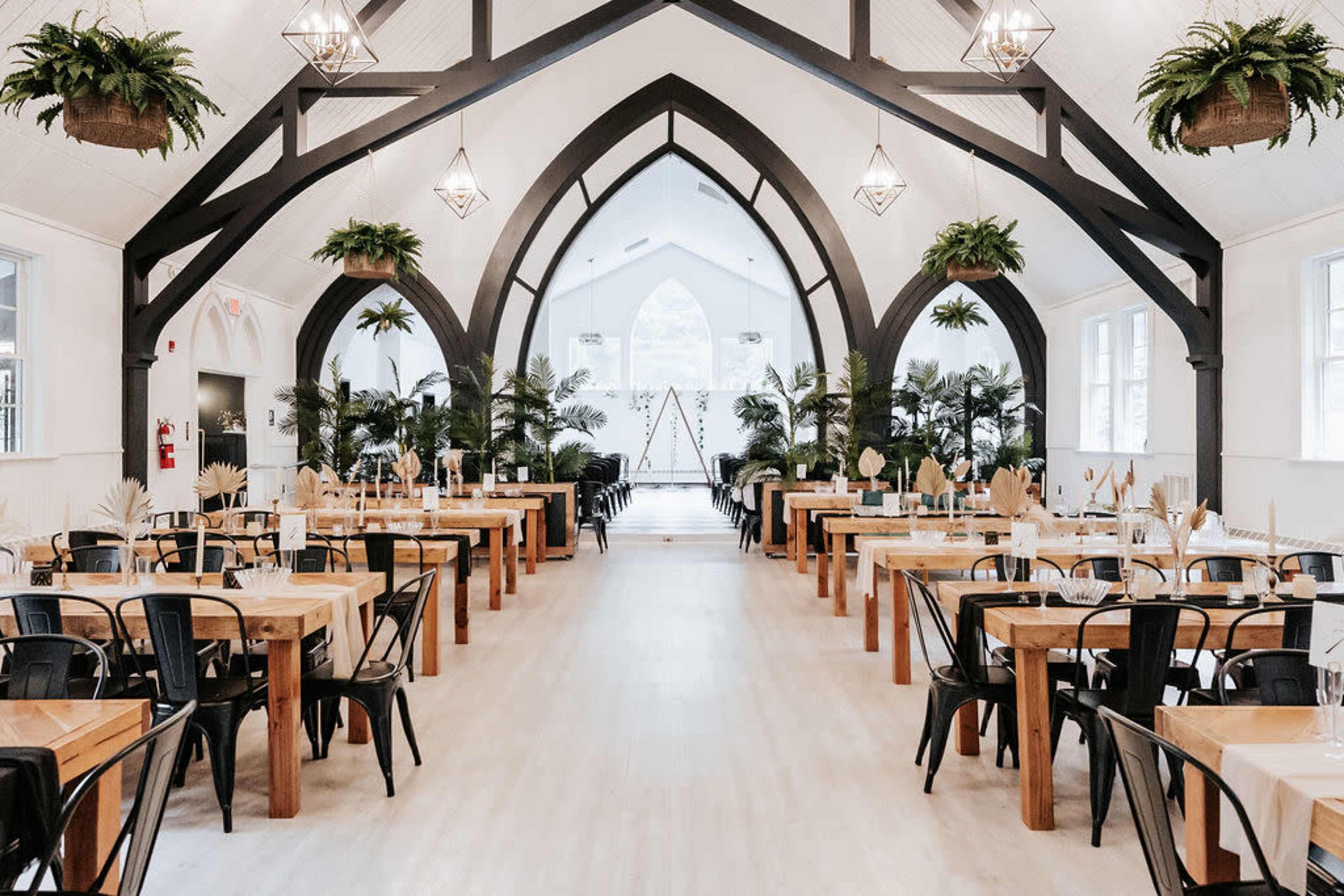 The image shows a spacious dining hall with wooden tables and black chairs, featuring arched ceilings and decorative plants.