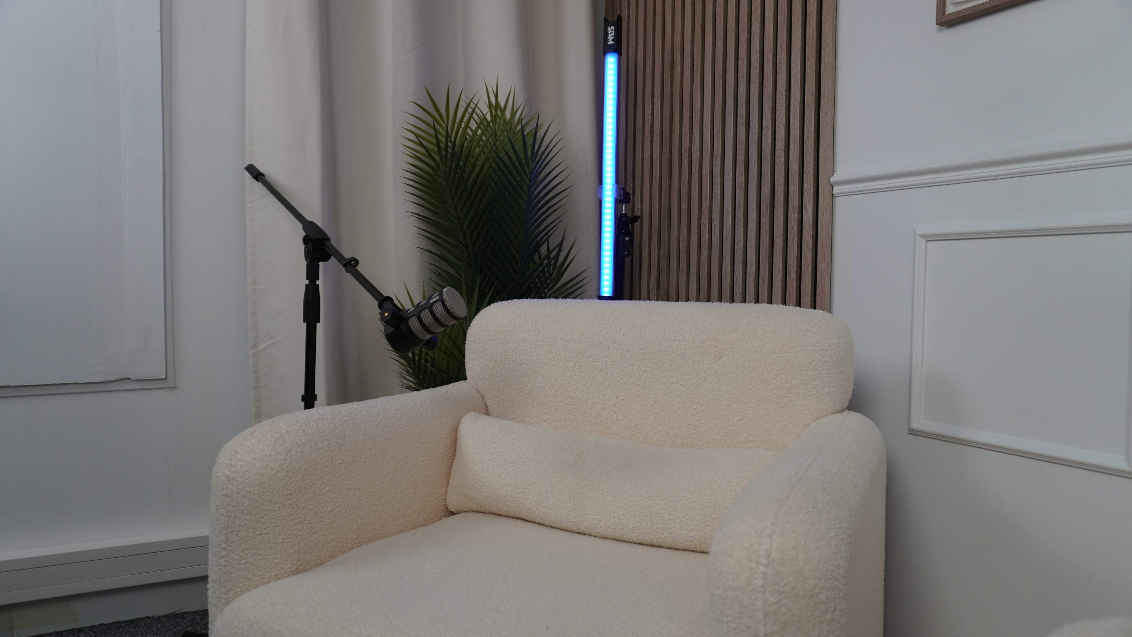 The image shows a light-colored, plush armchair next to a microphone on a stand and a potted plant in a well-lit indoor setting.