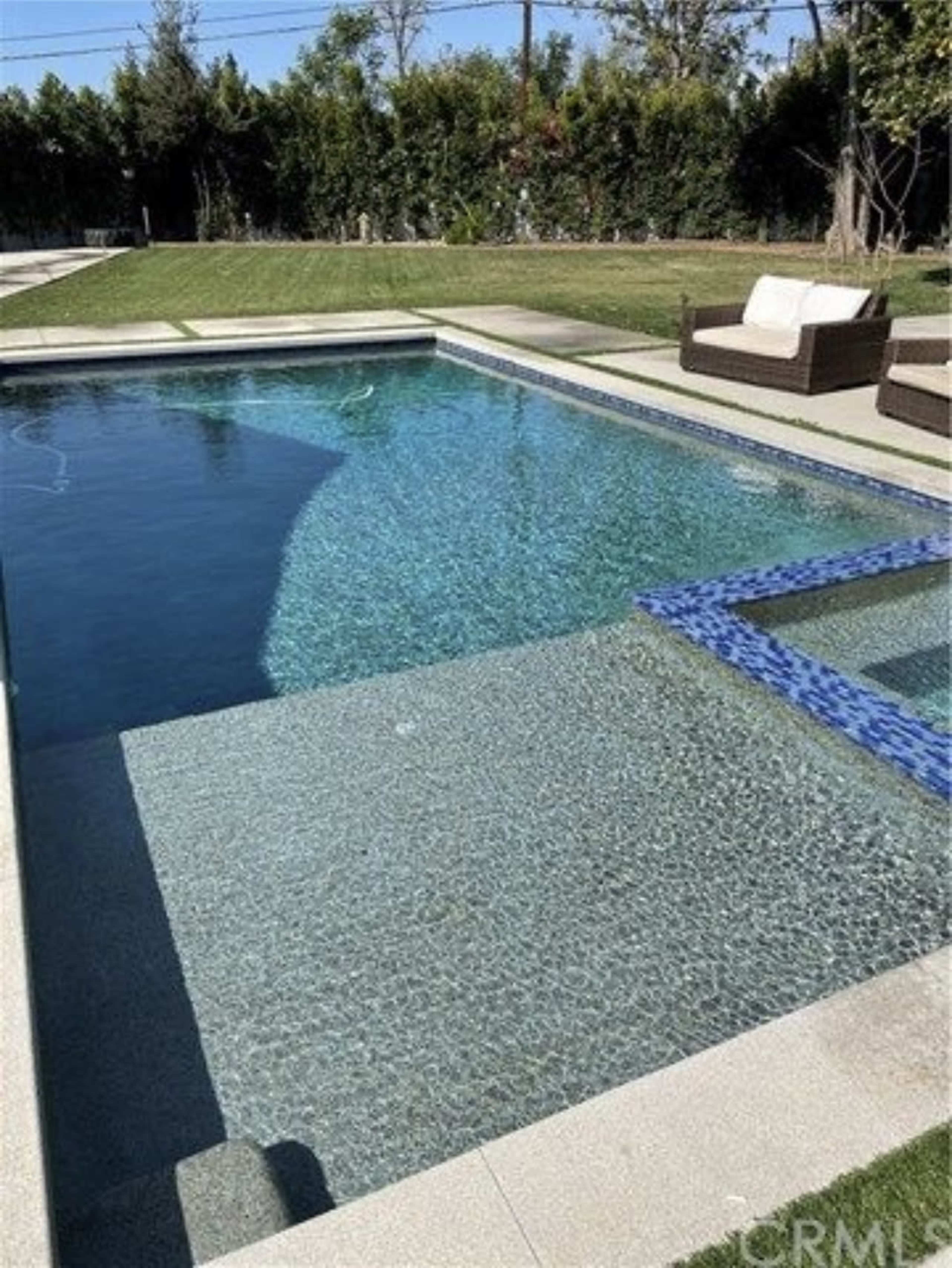 A rectangular swimming pool with clear water, surrounded by a manicured lawn and two lounge chairs nearby.