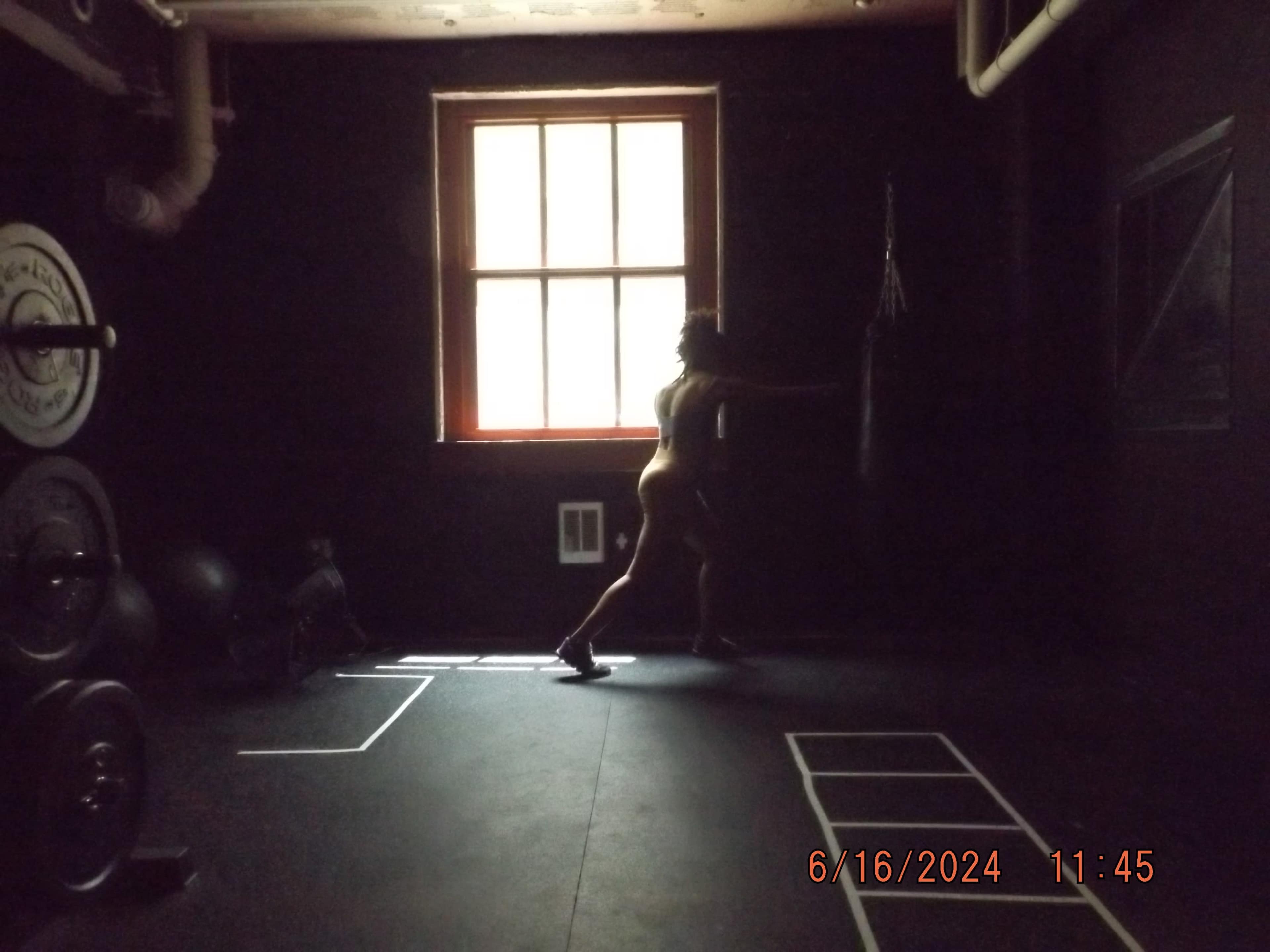 A silhouetted figure trains in a dimly lit gym with weights and a punching bag visible in the background.