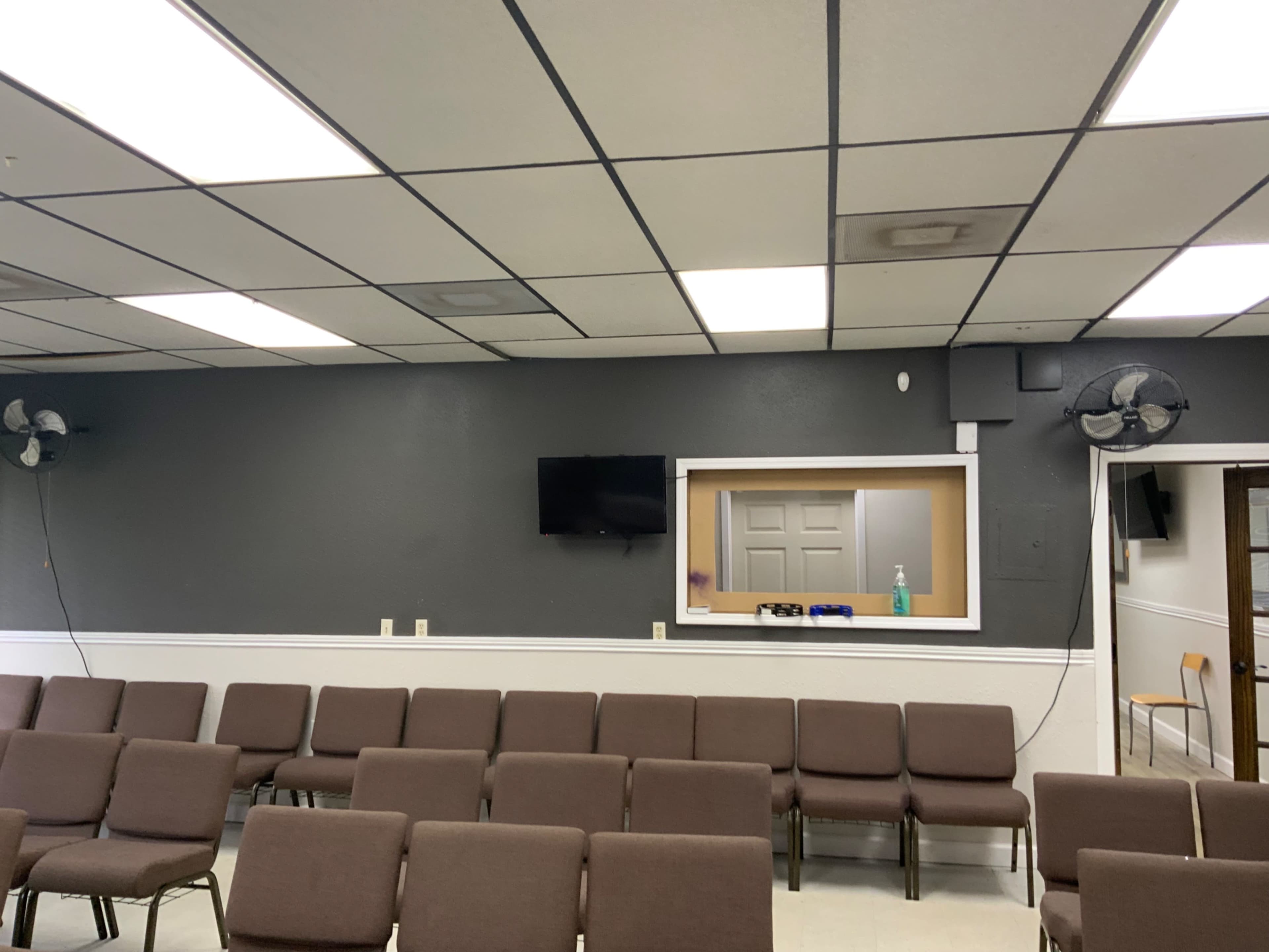 The image shows a seating area in a room with gray walls, a television mounted on the wall, and a small window to another room.