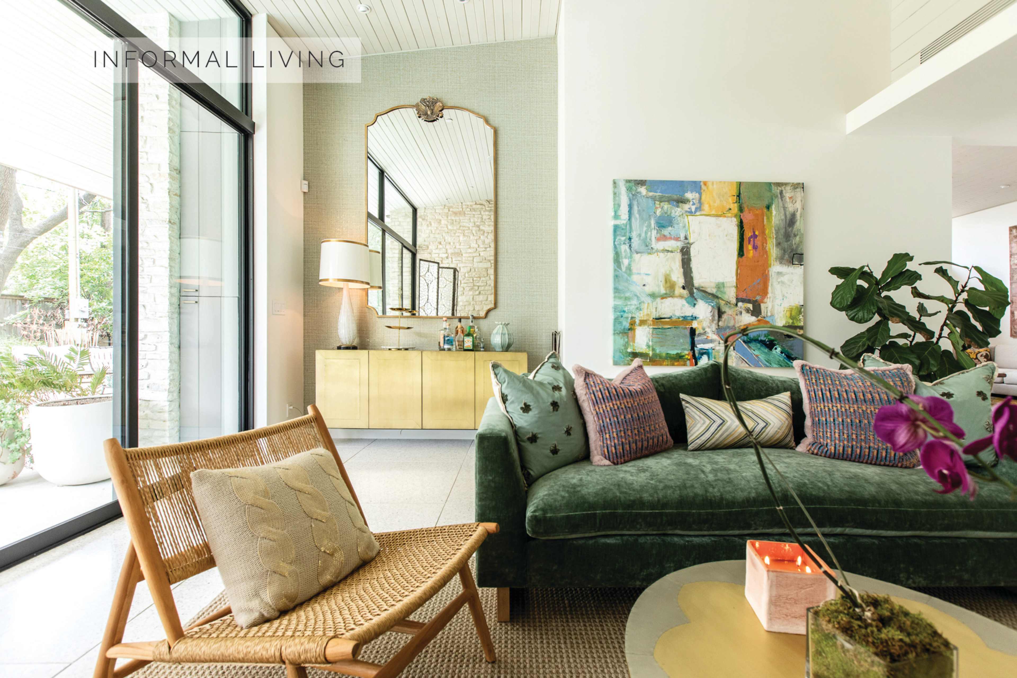 A modern living room featuring a green sofa with decorative pillows, a wooden chair, a glass coffee table, and large windows letting in natural light.